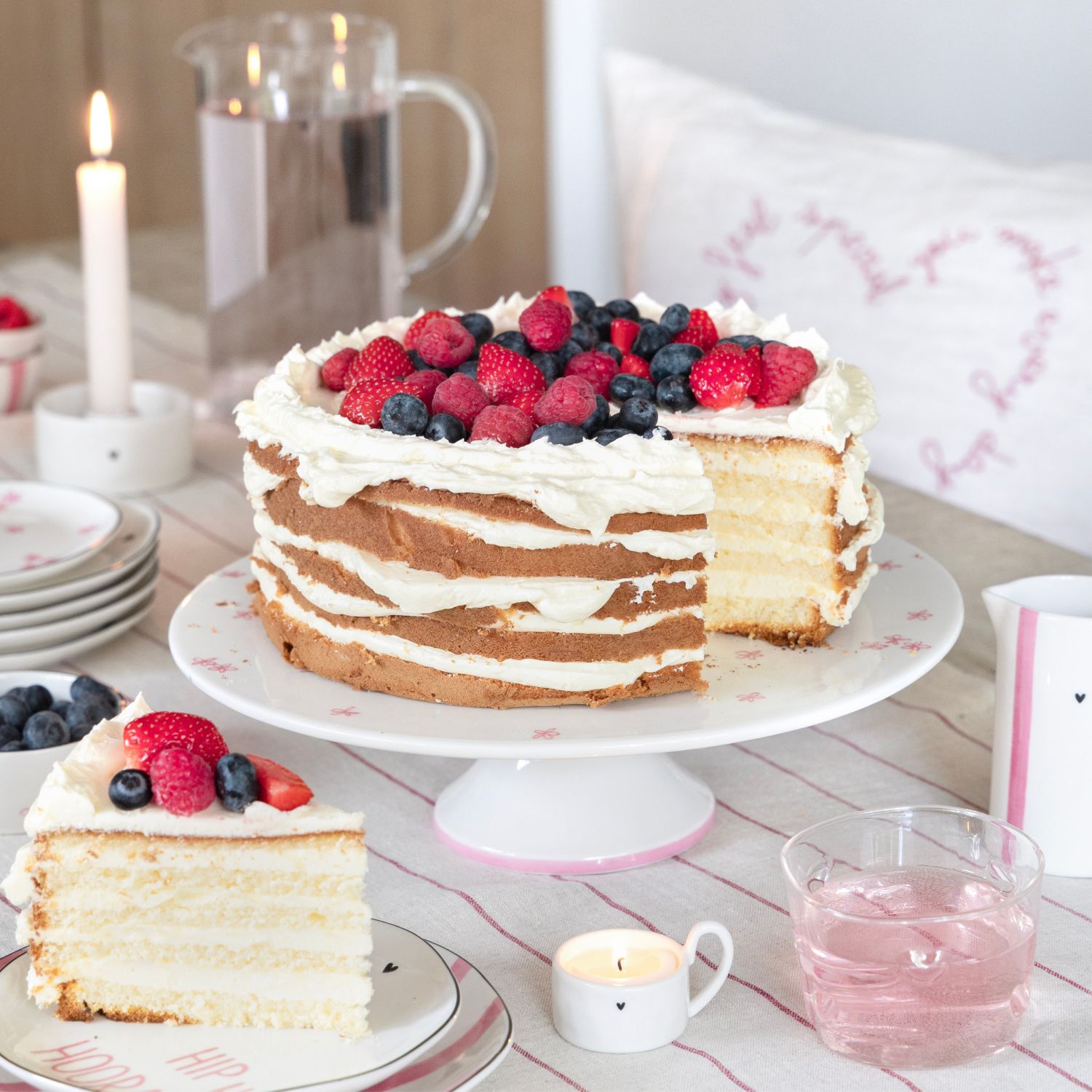 Anschnitt einer Sahnetorte mit Beeren auf Tortenplatte, Kuchenstück auf Teller daneben