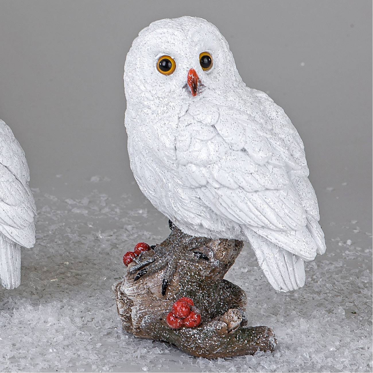 Eine weiße Eule mit großen, gelben Augen sitzt auf einem Ast, umgeben von glitzerndem Schnee und rot
