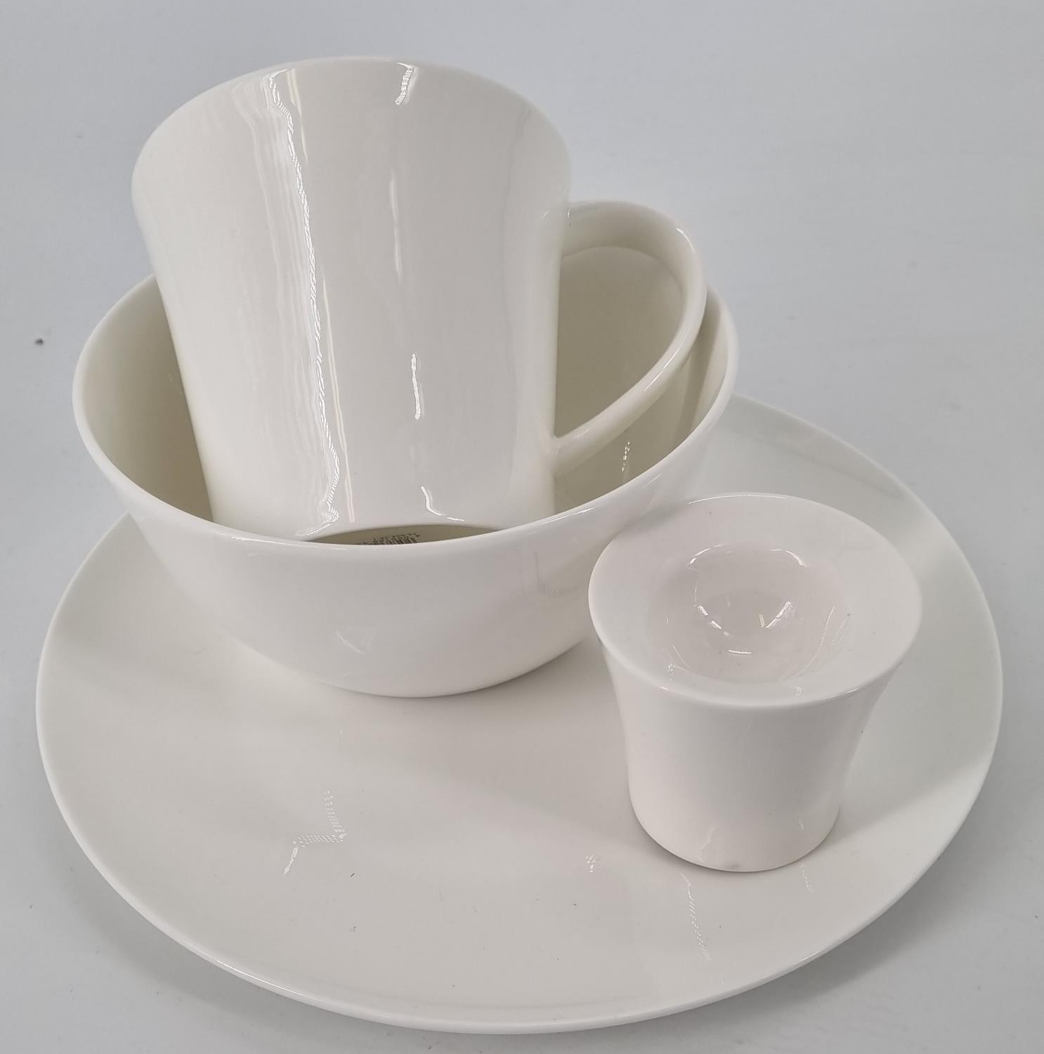 Ein Set aus weißen Tassen und Schalen, gestapelt auf einem flachen Teller. Die Formen sind schlicht und modern.