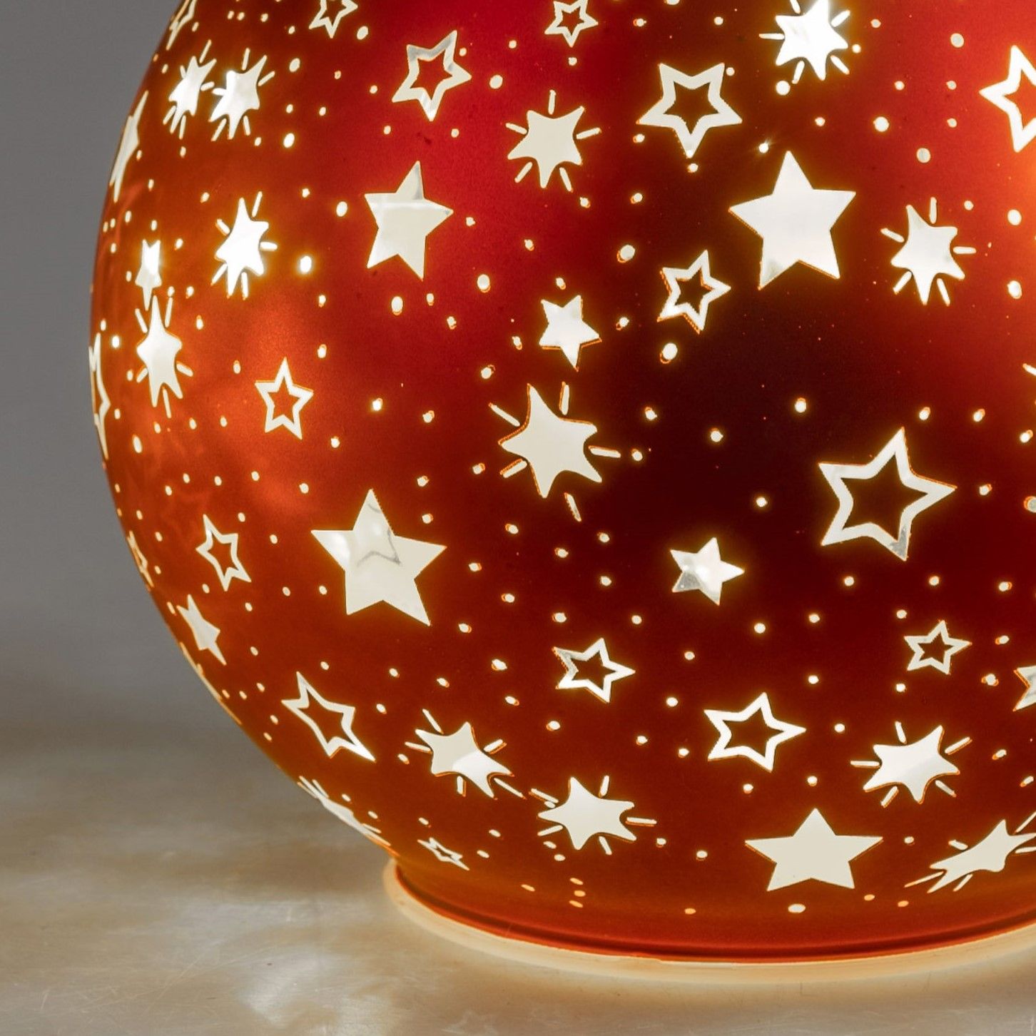 Runde, rote Lampe mit durchbrochenen Sternenmotiven, die warmes Licht abstrahlt. Hintergrund in neut