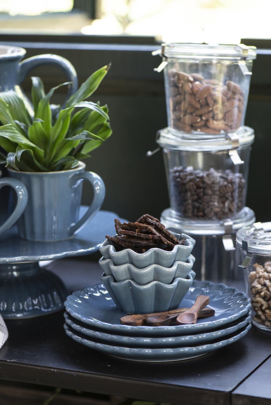Ein Tisch mit blauen Tellern, einer Pflanze in einer Tasse, Schalen und Gläsern mit Nüssen und Kaffeebohnen.