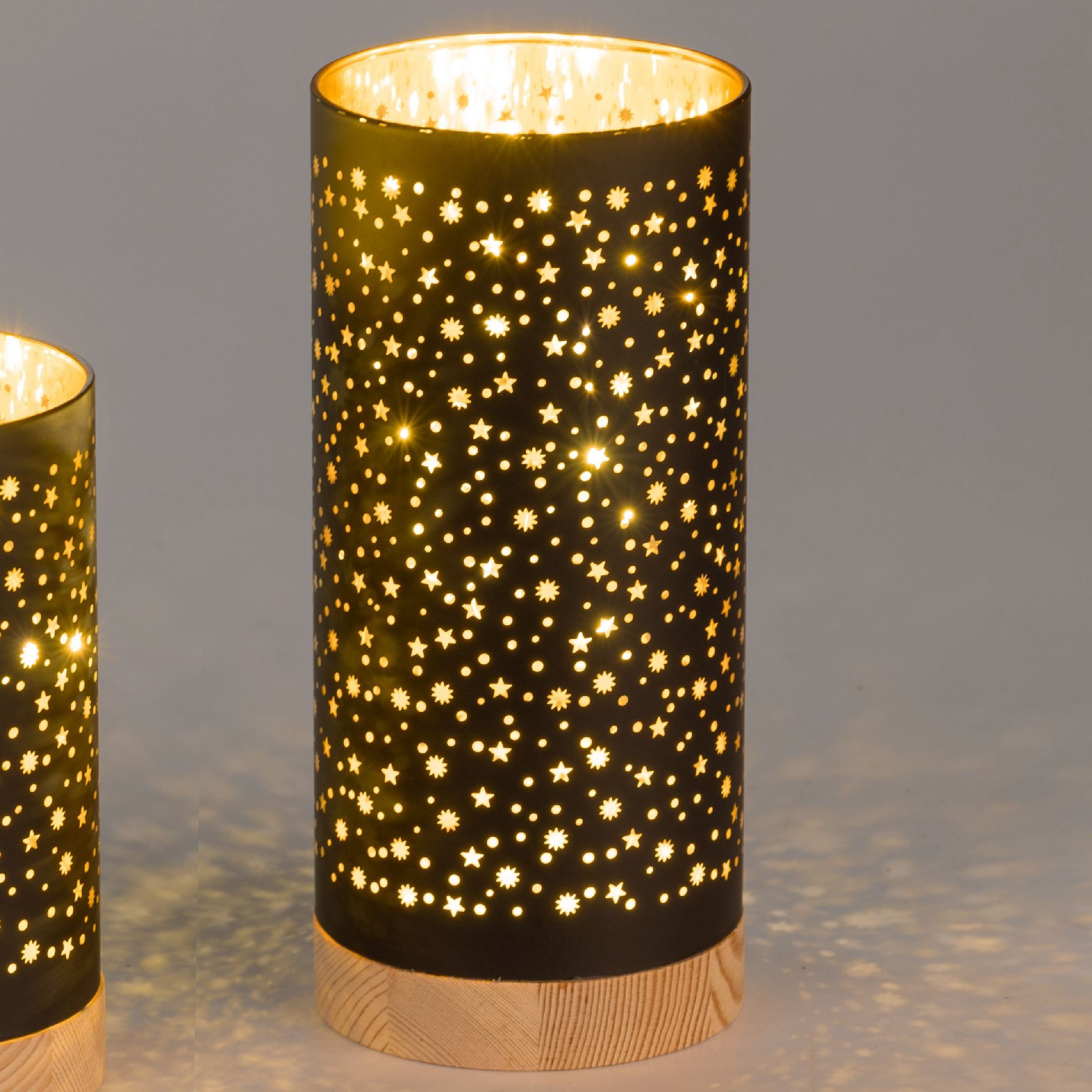 Zwei zylindrische Lampen mit perforierten Mustern, die warmes Licht abstrahlen und einen Sternenhimm