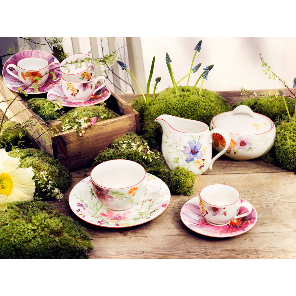 Tee-Service aus Porzellan mit bunten Blumenmotiven, platziert auf Moos und Holz, umgeben von Pflanzen.