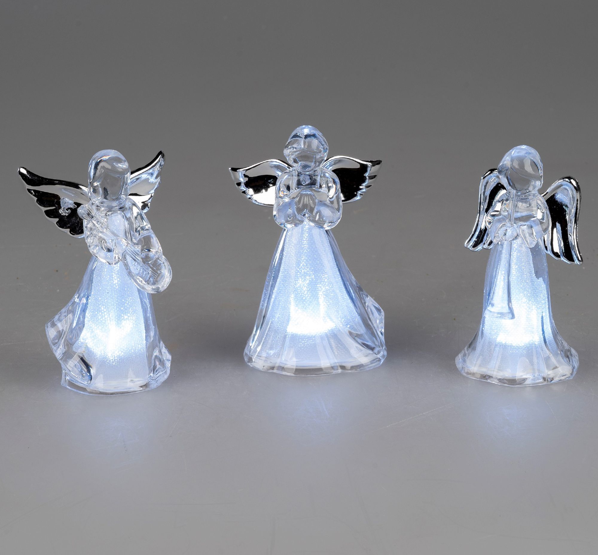 Drei gläserne Engel mit leuchtenden Körpern stehen nebeneinander. Sie haben Flügel und sind in versc