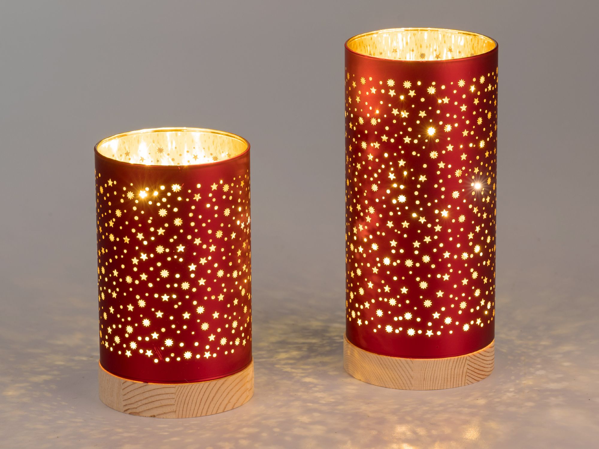 Zwei rote Lampen mit Sternenmustern, die warmes Licht ausstrahlen auf Holzsockel