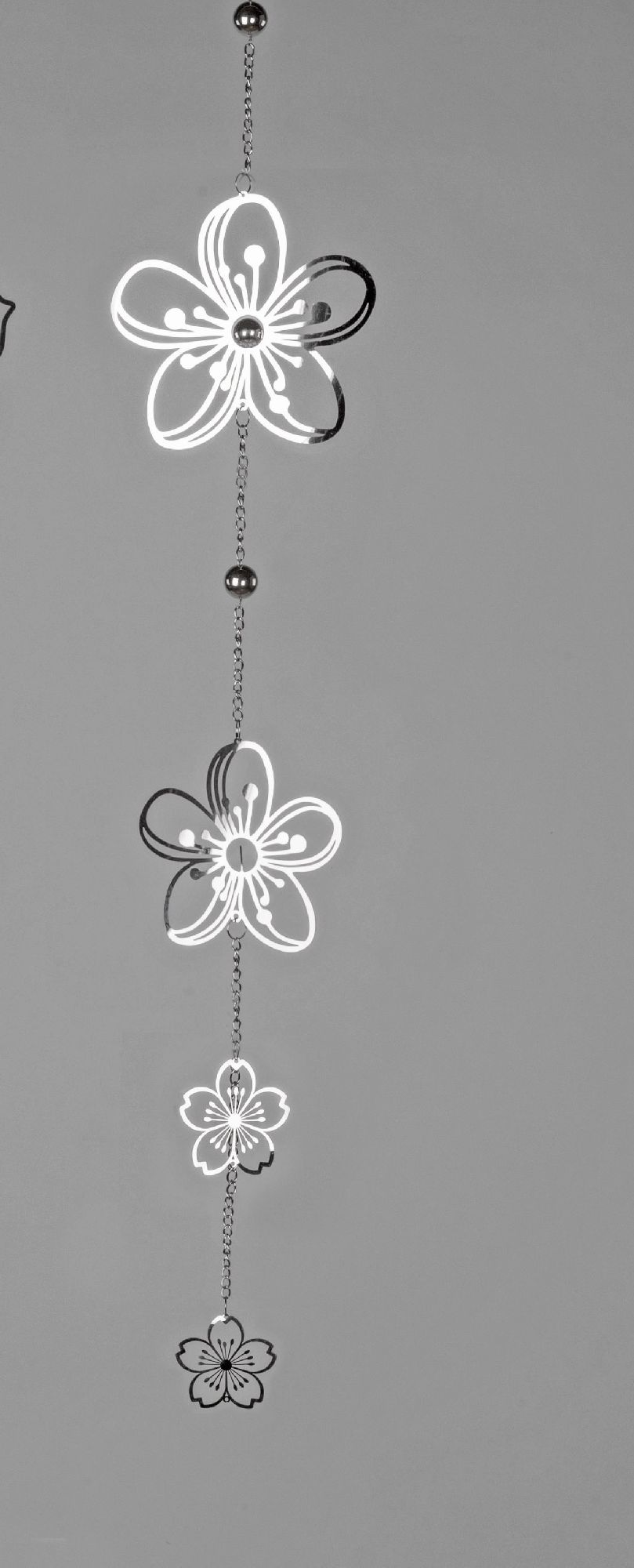 Drei stilisierte Blumen aus transparentem Material hängen an einer Kette vor einem grauen Hintergrund.