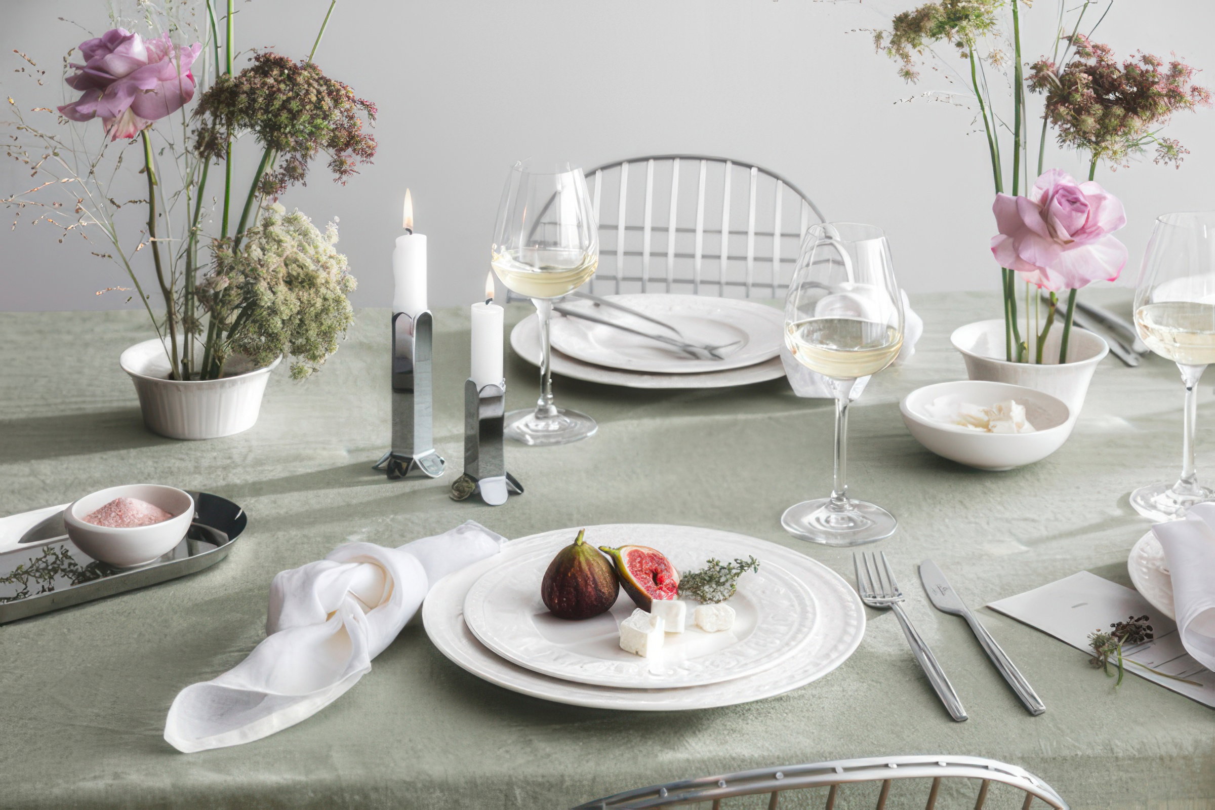 Tischgedeck mit Tellern, Gläsern, Kerzen und Blumenarrangements. Auf dem Teller liegen Feigen und Käse.