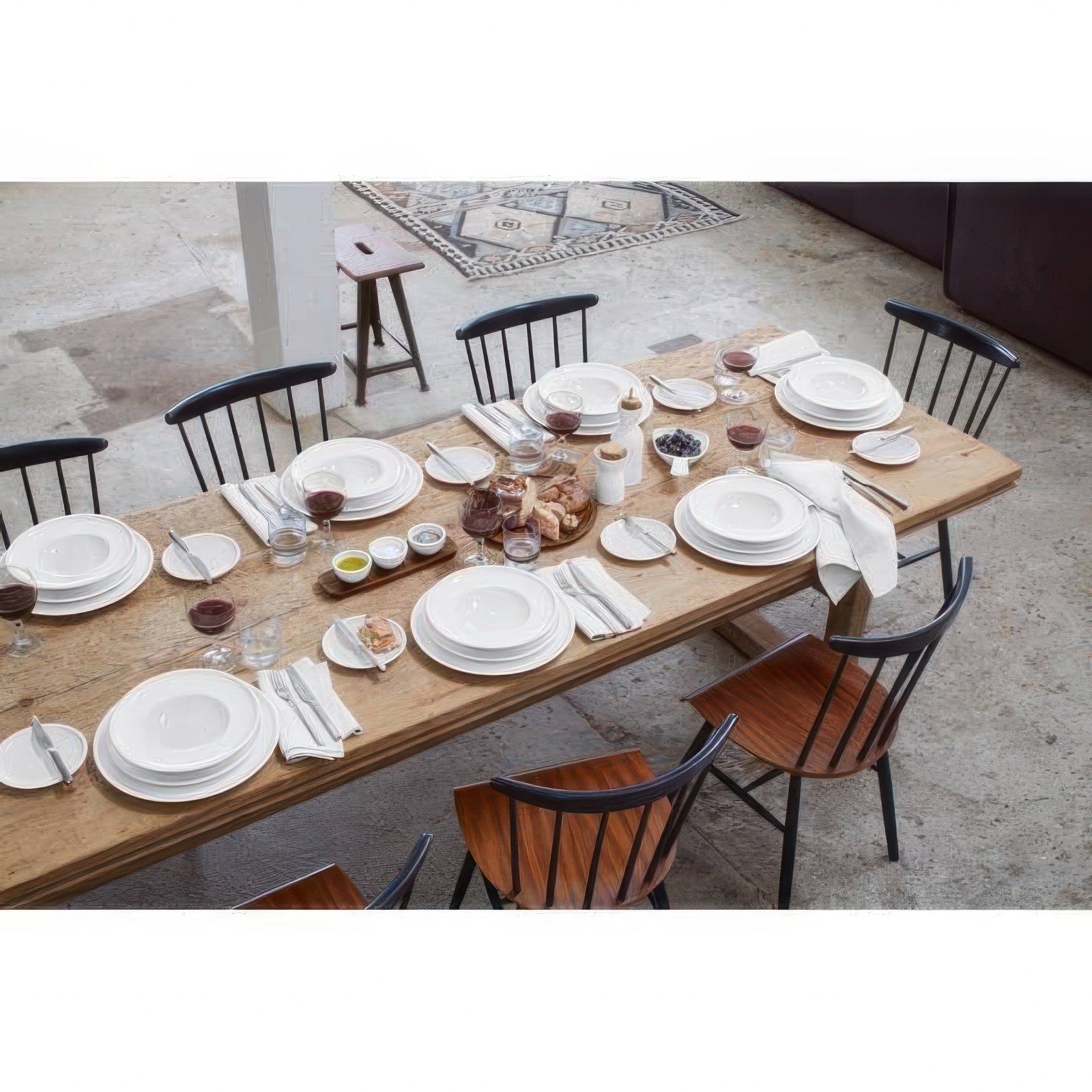Ein gedeckter Holztisch mit weißen Tellern, Gläsern, Besteck und verschiedenen Speisen. Stühle sind um den Tisch angeordnet.