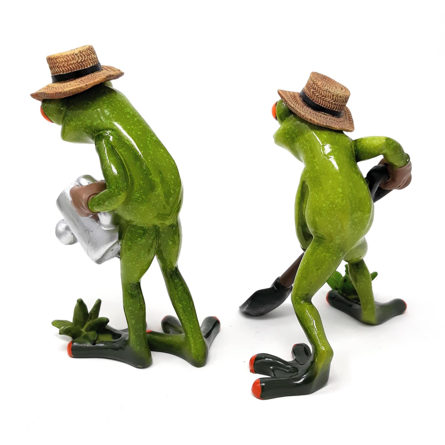Zwei grüne Froschfiguren mit Strohhüten, eine hält eine Kiste, die andere einen Spaten. Beide stehen