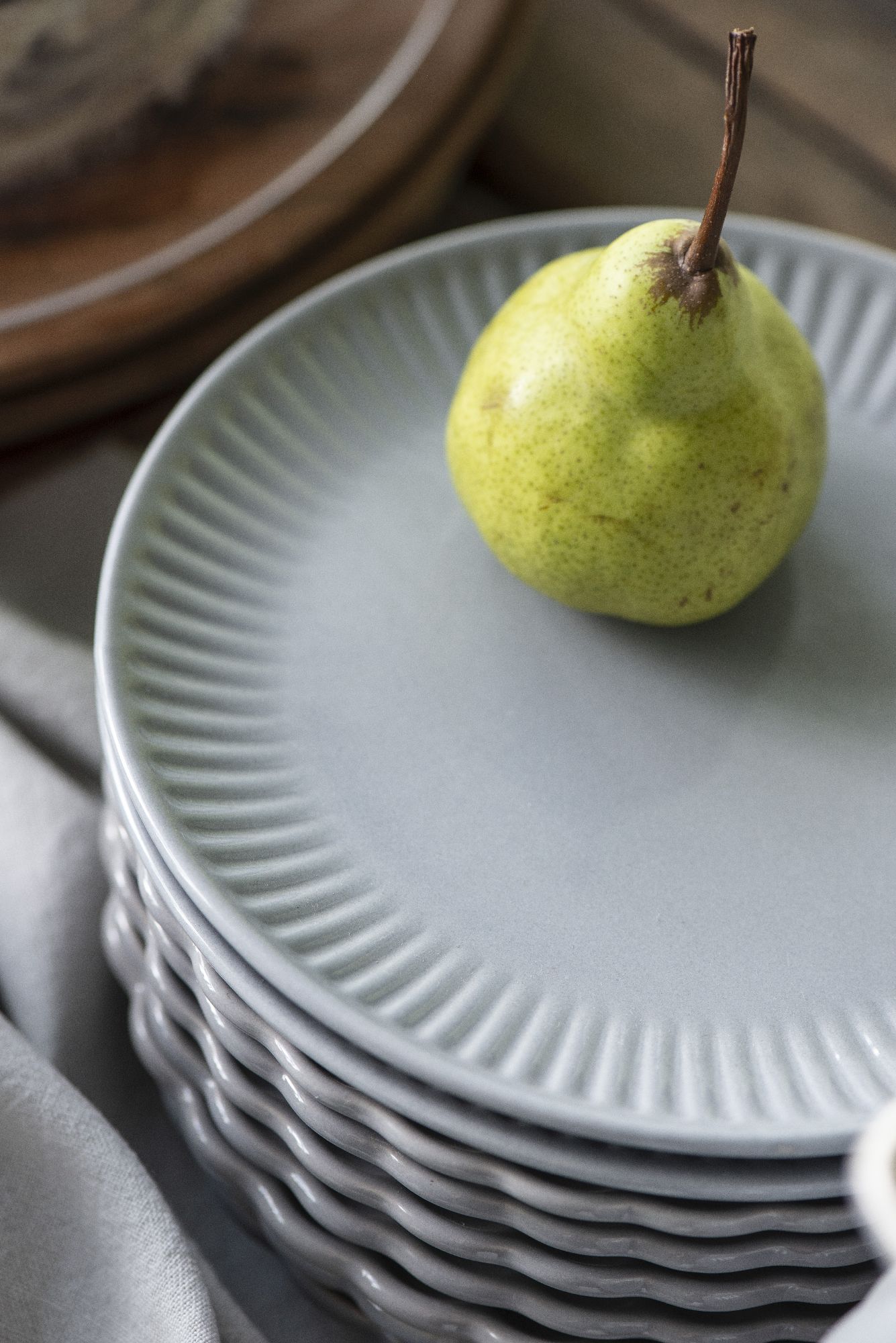 Ein grüner Birne liegt auf einem grauen Teller, der auf einem Stapel weiterer Teller platziert ist. Im Hintergrund ist Holz sichtbar.
