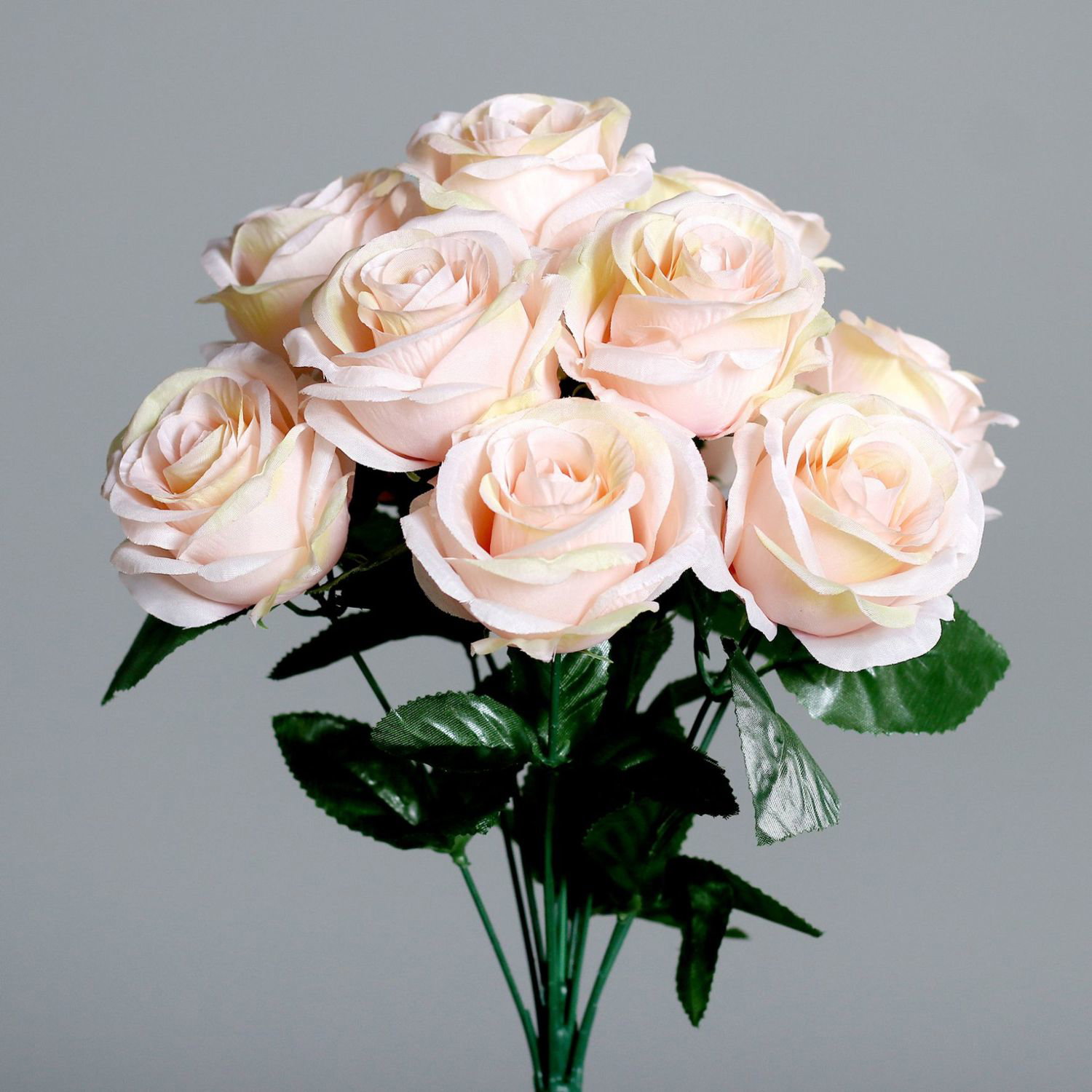 Strauß aus zart rosafarbenen Rosen mit grünen Blättern vor grauem Hintergrund