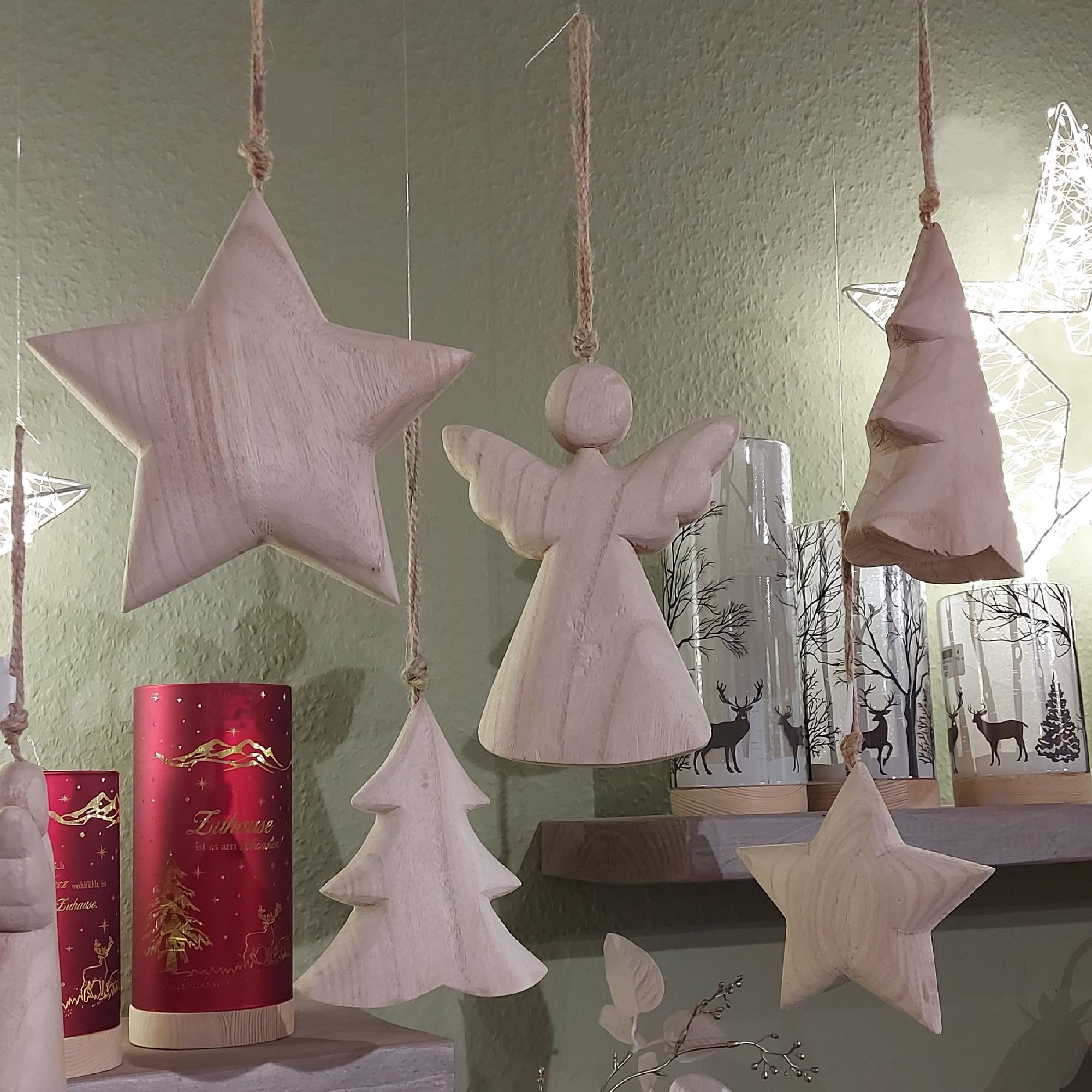 Hängende Holzfiguren: ein Stern, ein Engel, ein Tannenbaum und ein weiterer Stern. Im Hintergrund si