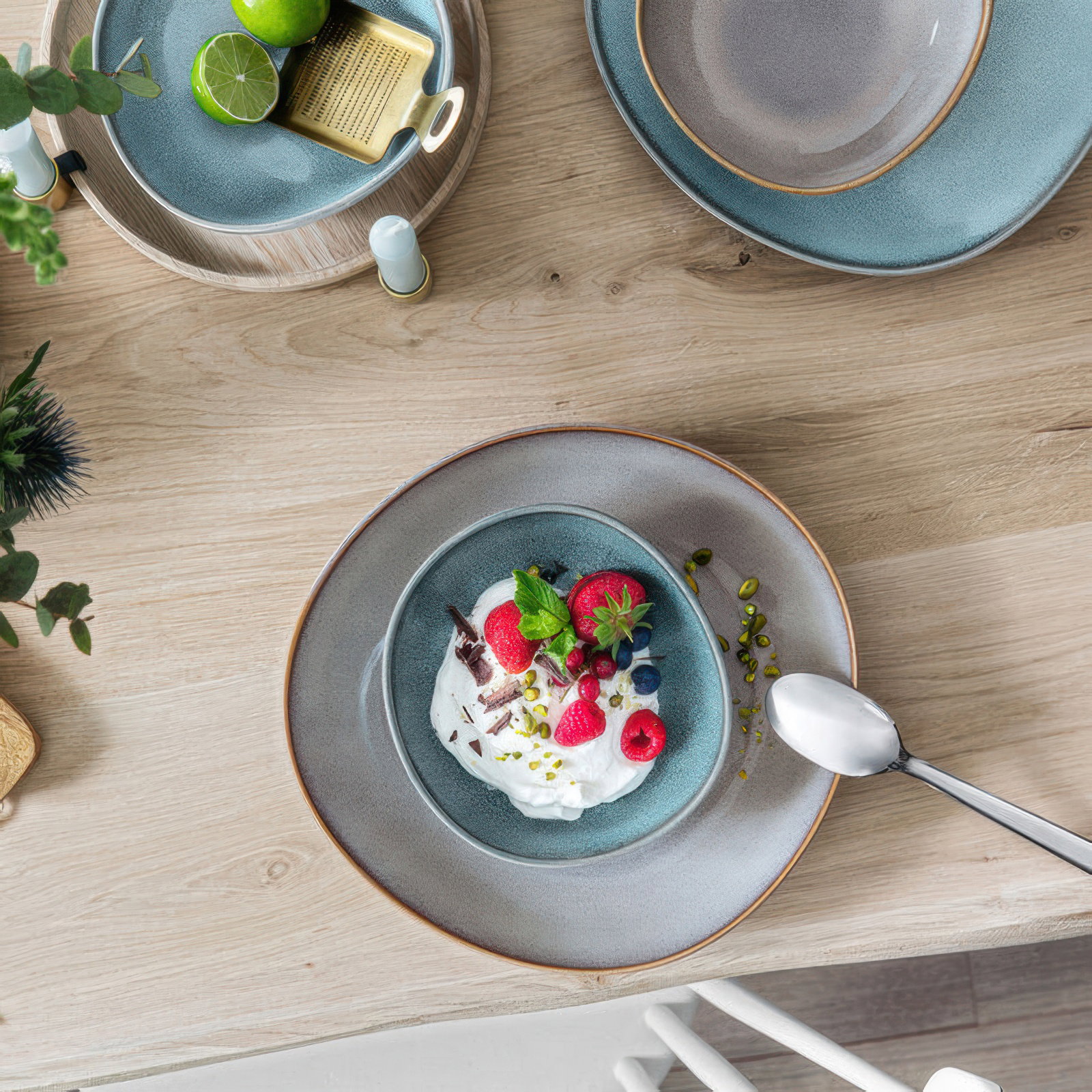 Tisch mit Tellern und Schalen. In einer Schale befindet sich Joghurt mit Beeren, Pistazien und Minze
