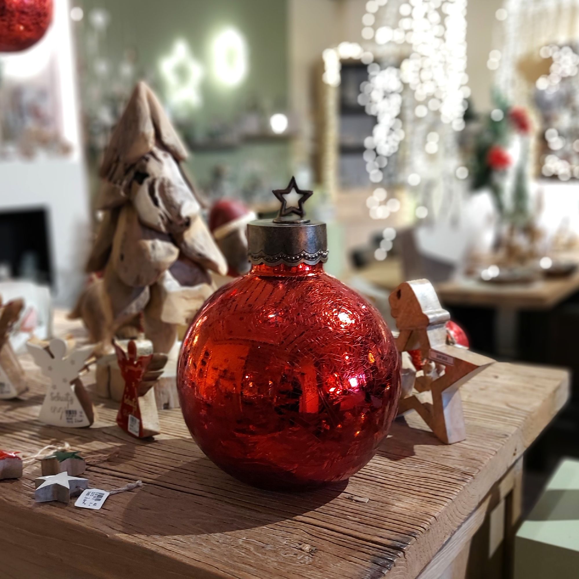 Rote Weihnachtskugel mit Sternverschluss auf einem Holztisch, umgeben von Holzfiguren und einem klei