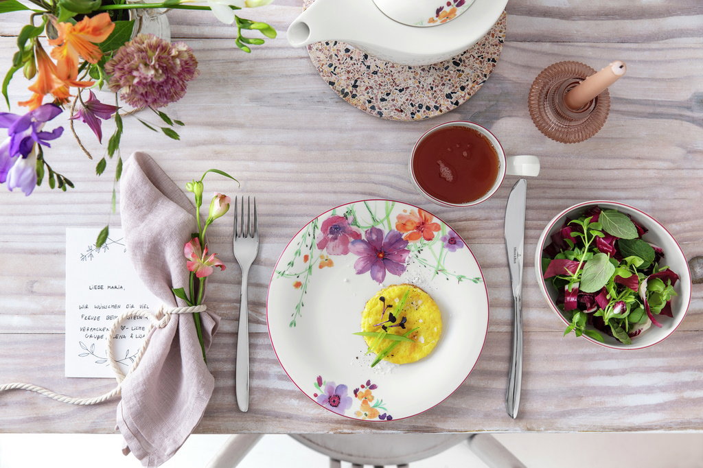 Ein gedeckter Tisch mit einem bunten Blumenstrauß, einer Tasse Tee, einem Teller mit einem Gericht u