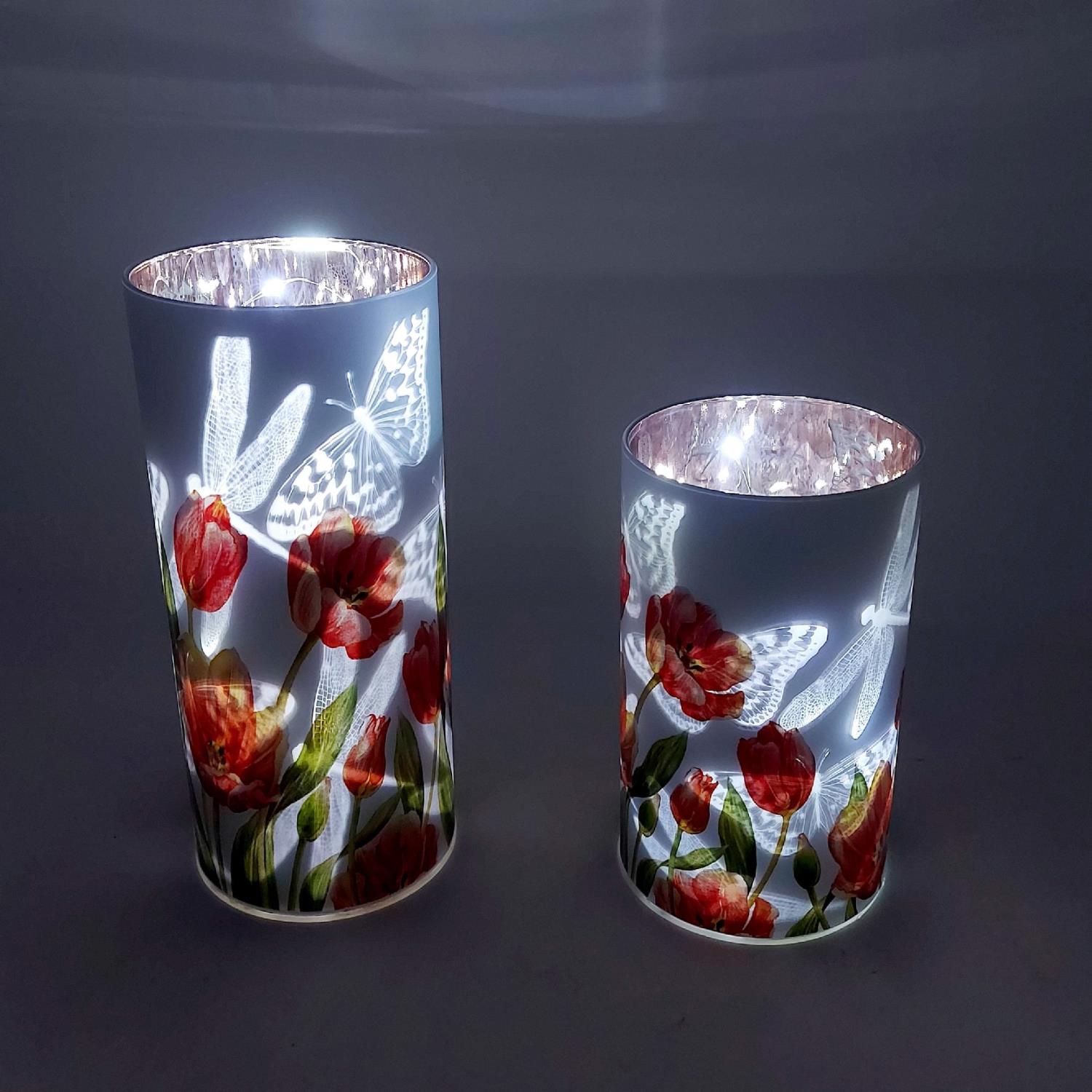 Zwei dekorative Kerzenhalter mit floralen Motiven und Schmetterlingen, beleuchtet von innen, auf ein