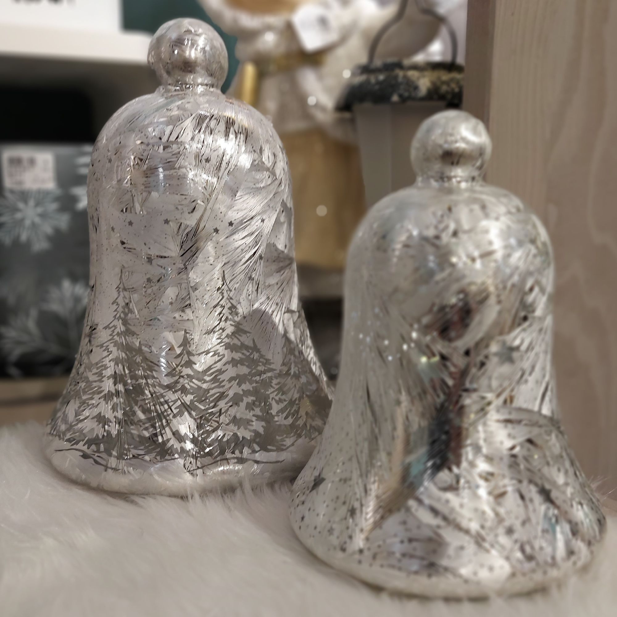 Zwei silberne Glöckchen mit glitzernder Oberfläche und einem Muster von Bäumen, auf einem weißen, fl