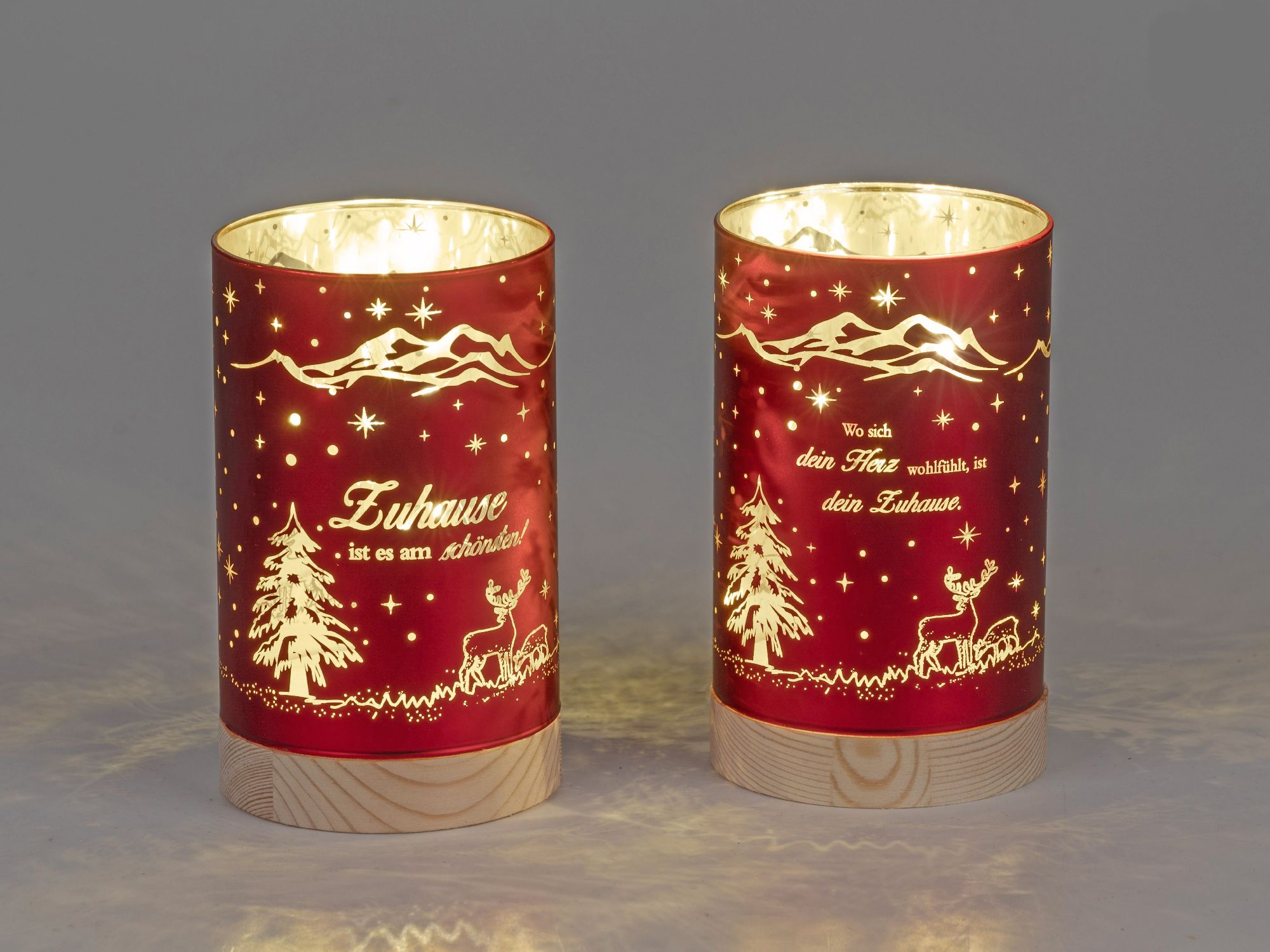 Zwei rote Laternen mit Weihnachtsmotiven, darunter Bäume und Rehe, leuchten sanft. Auf jeder Laterne