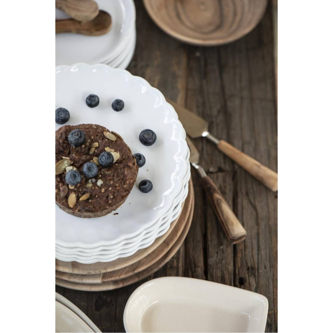 Ein Stapel weißer Teller mit einem runden Kuchen, garniert mit Blaubeeren und Kürbiskernen, auf einem Holztisch.