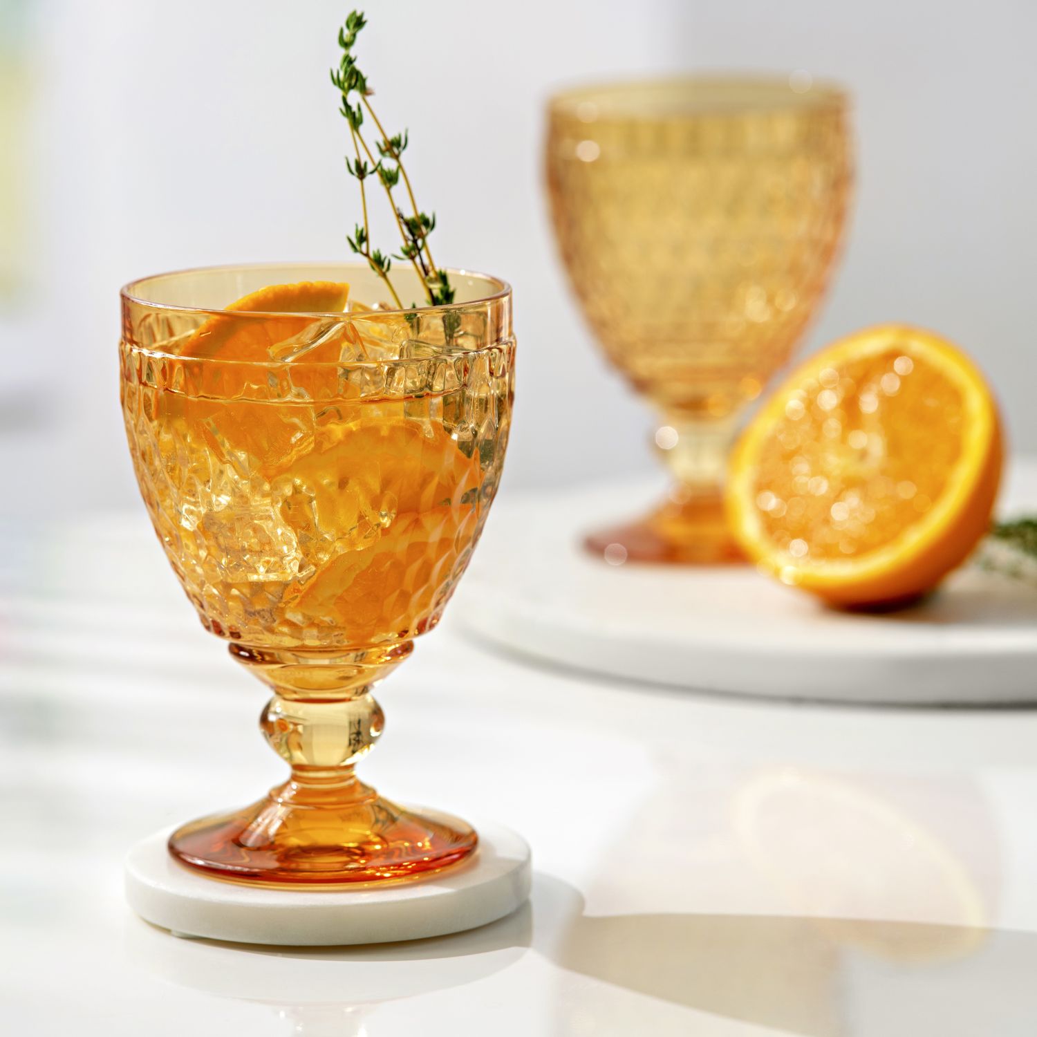 Ein Glas mit Orangenscheiben und Thymian auf einem weißen Untersetzer