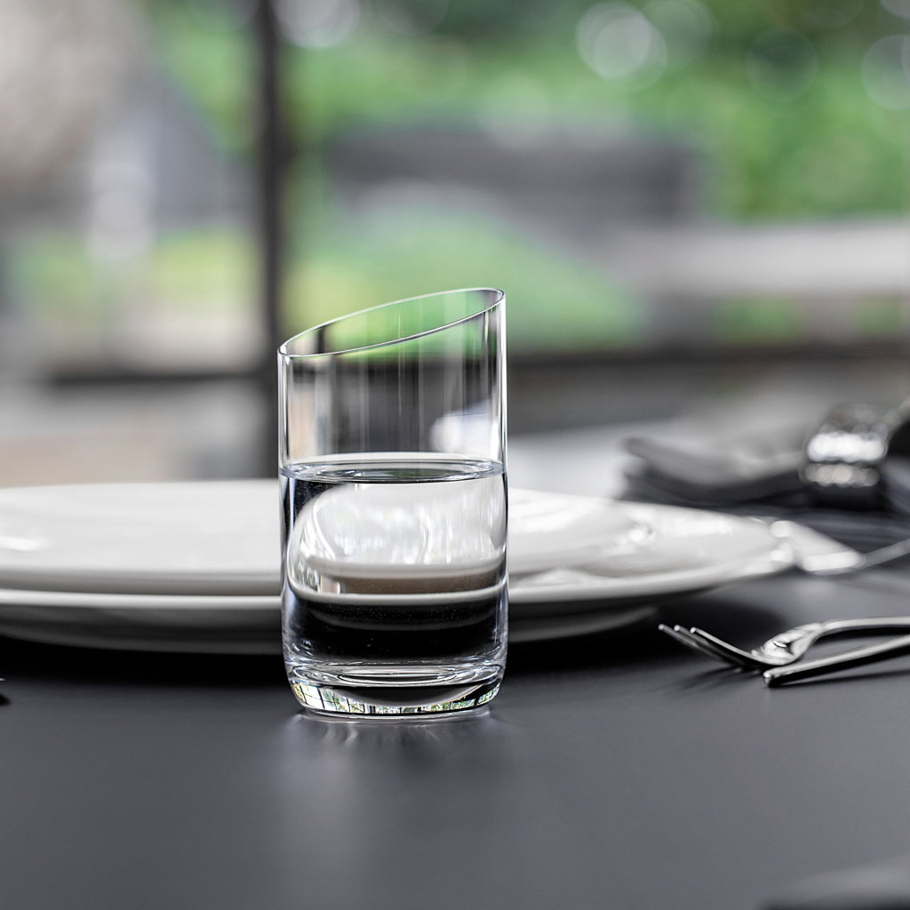 Ein Glas mit Wasser steht auf einem Tisch neben einem Teller und Besteck