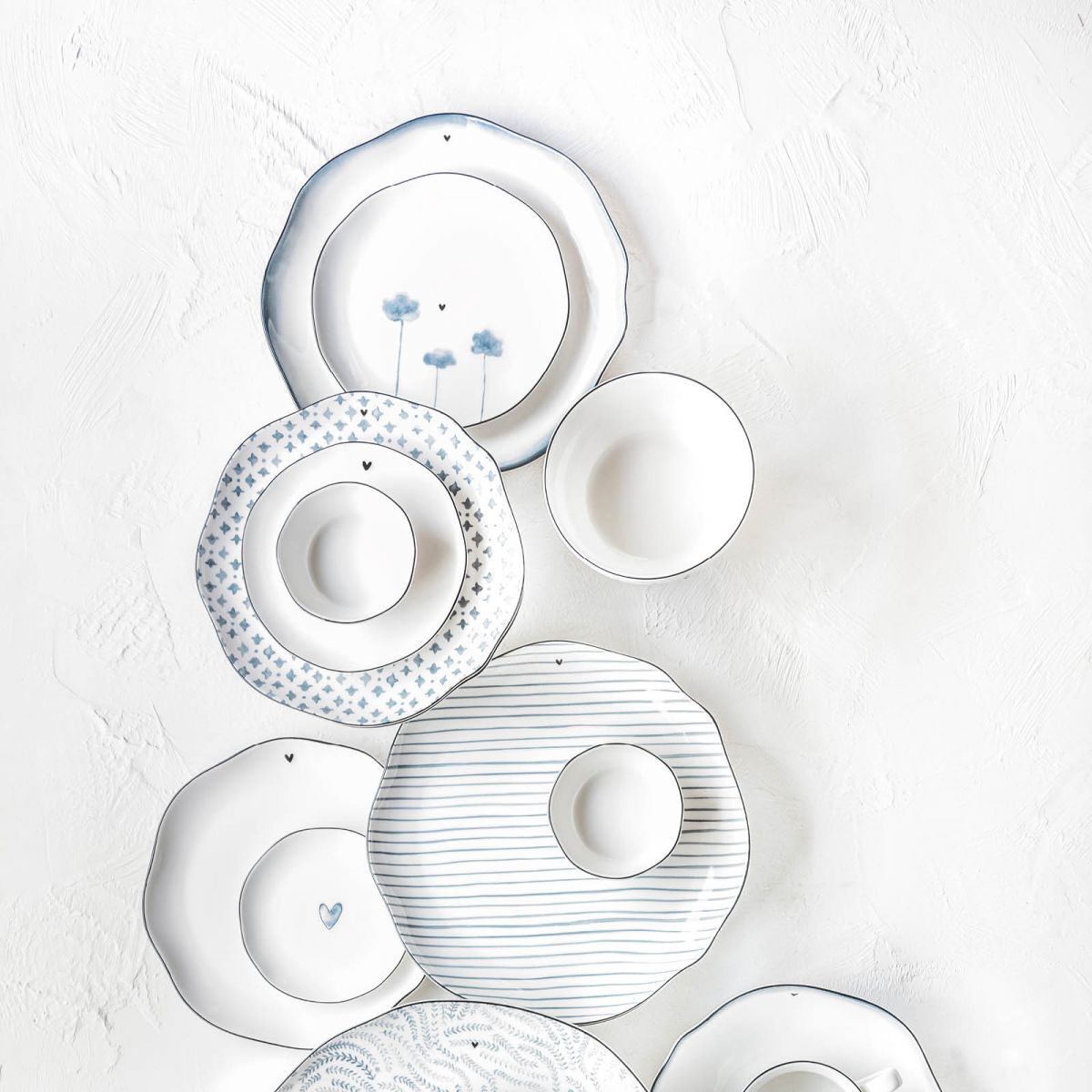 Eine Anordnung von Tellern und Schalen in verschiedenen Größen und Designs auf einem hellen Hintergrund.