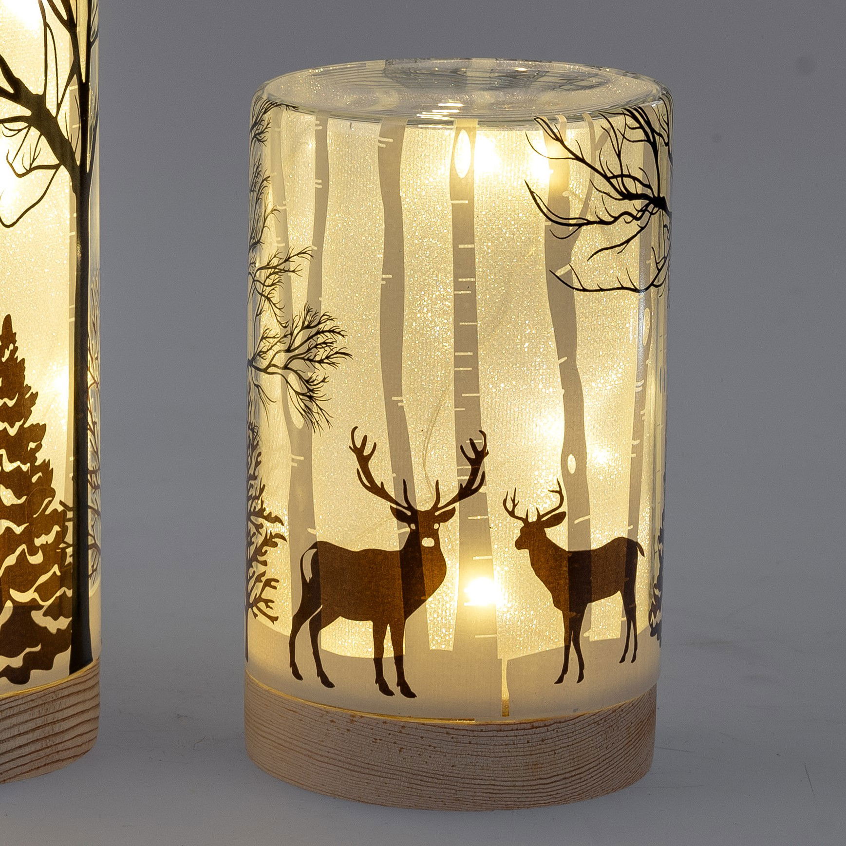Dekorative Laterne mit transparentem Design, beleuchtet, zeigt Silhouetten von Bäumen und zwei Rehen