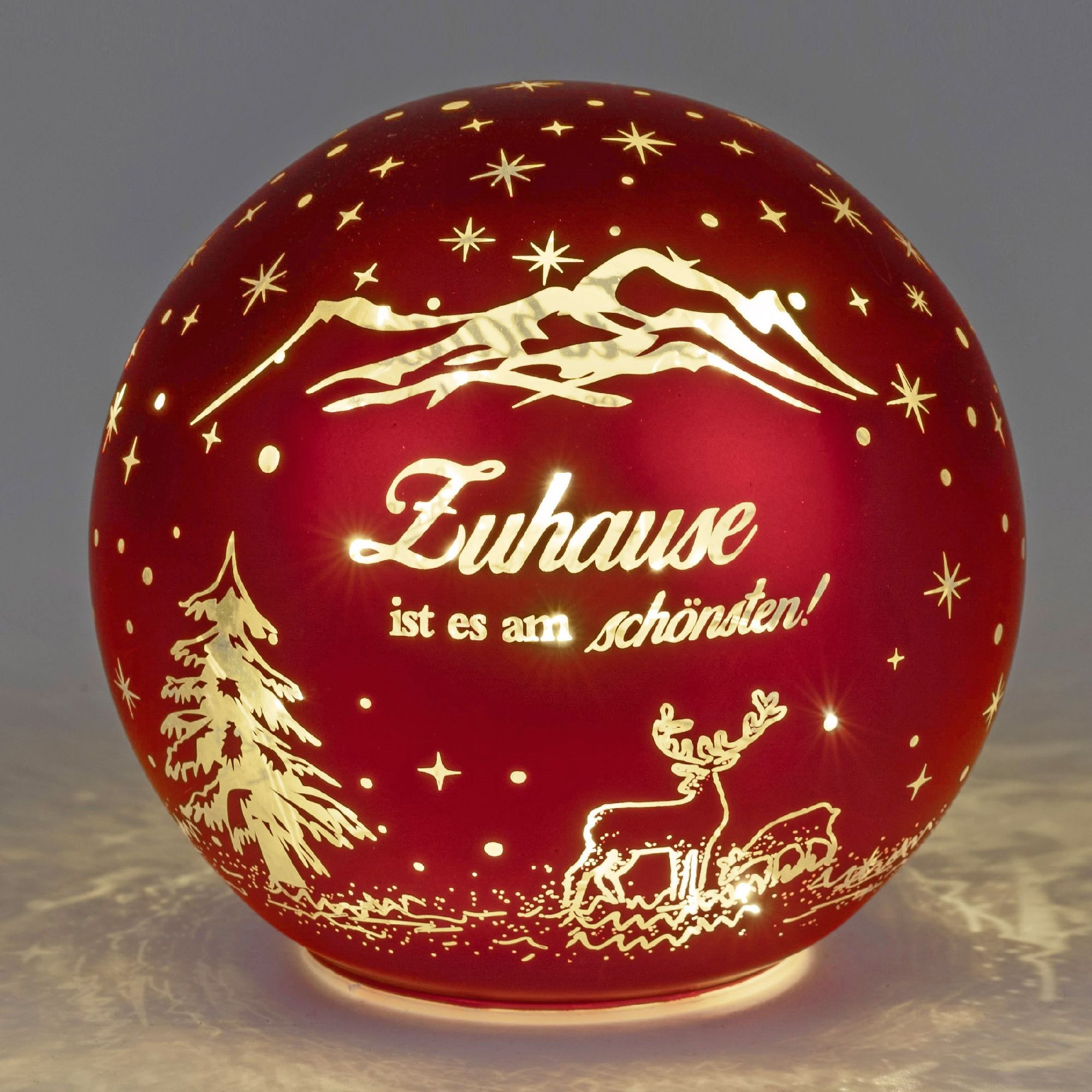 Rote Glaskugel mit goldenen Motiven: Berge, Tannenbaum, Reh und dem Schriftzug „Zuhause ist es am sc
