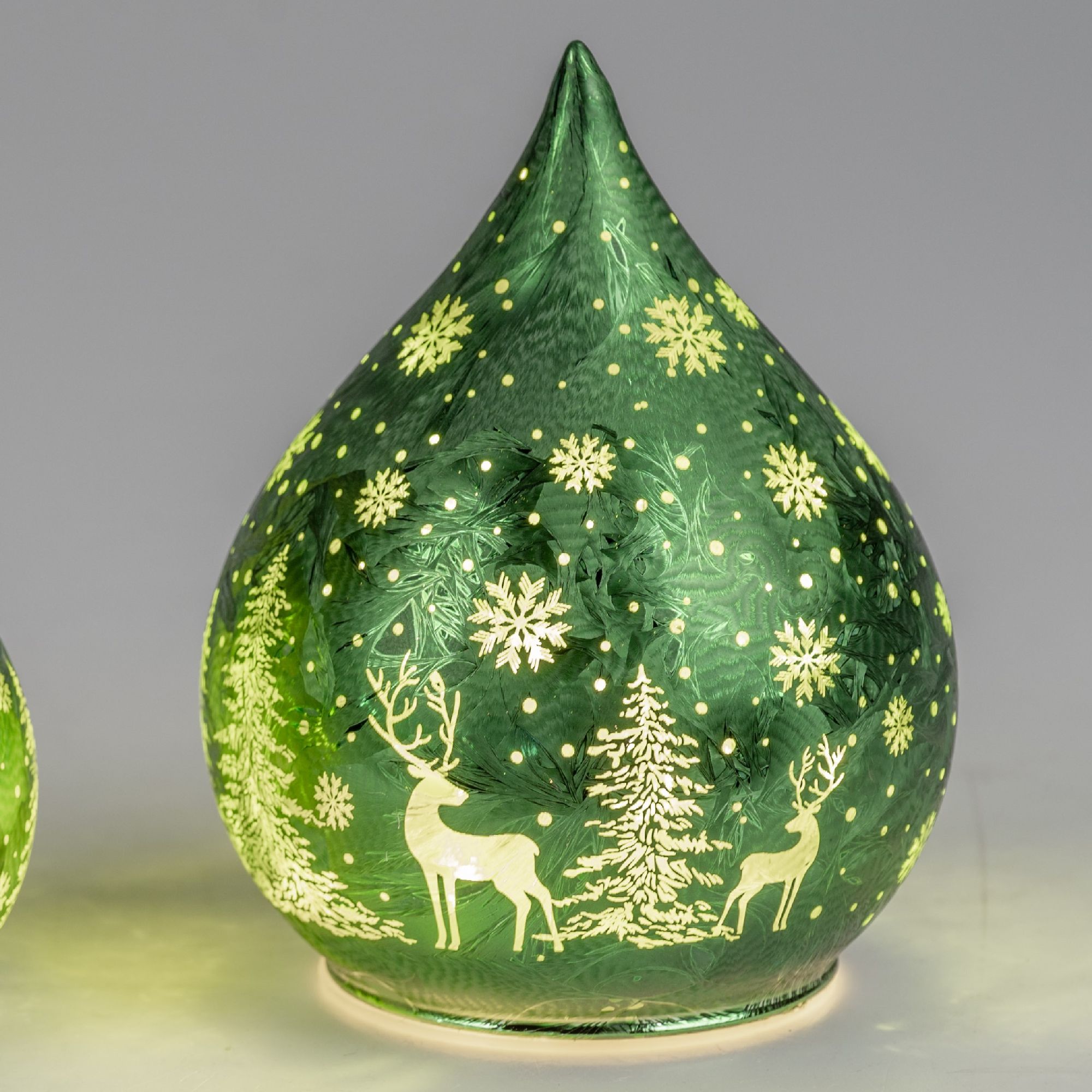 Grüne, tropfenförmige Lampe mit Schneeflocken- und Weihnachtsbaum-Motiven sowie zwei Rehen, die von