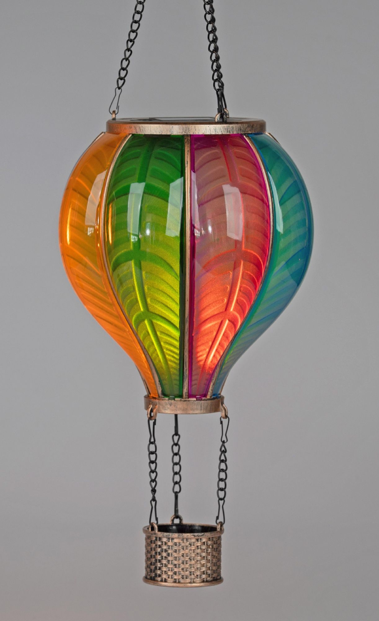 Bunte, gläserne Heißluftballon-Dekoration mit einem Korb, hängt an einer Kette vor einem grauen Hint