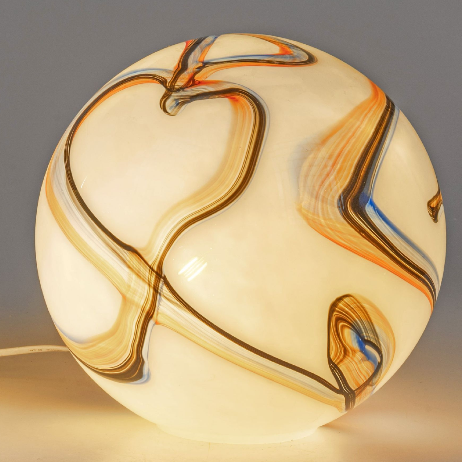 Runde Tischlampe aus milchigem Glas mit geschwungenen braun-orangen und blauen Linien