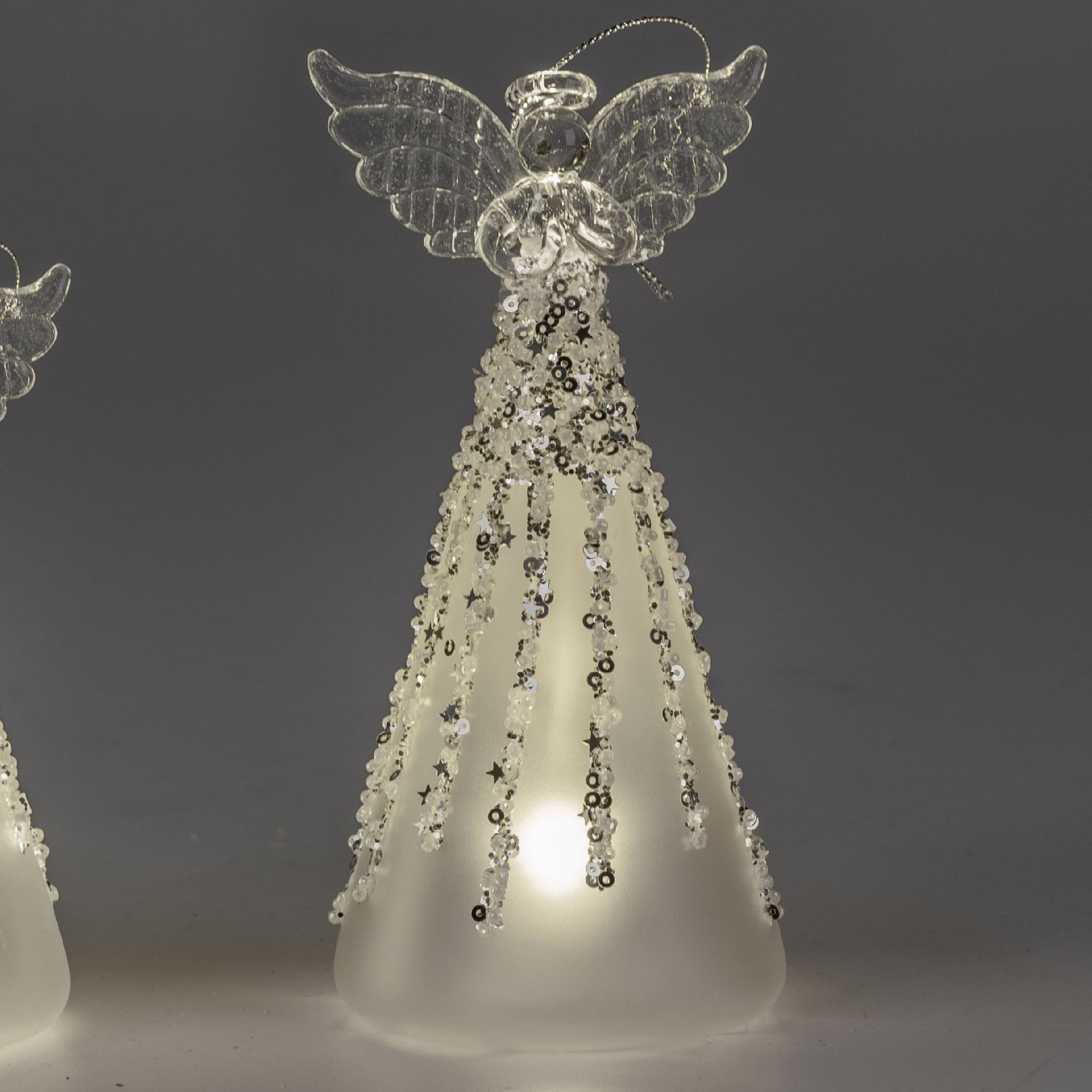 Zwei transparente Engel aus Glas mit glitzernden Verzierungen und einer leuchtenden Basis stehen vor