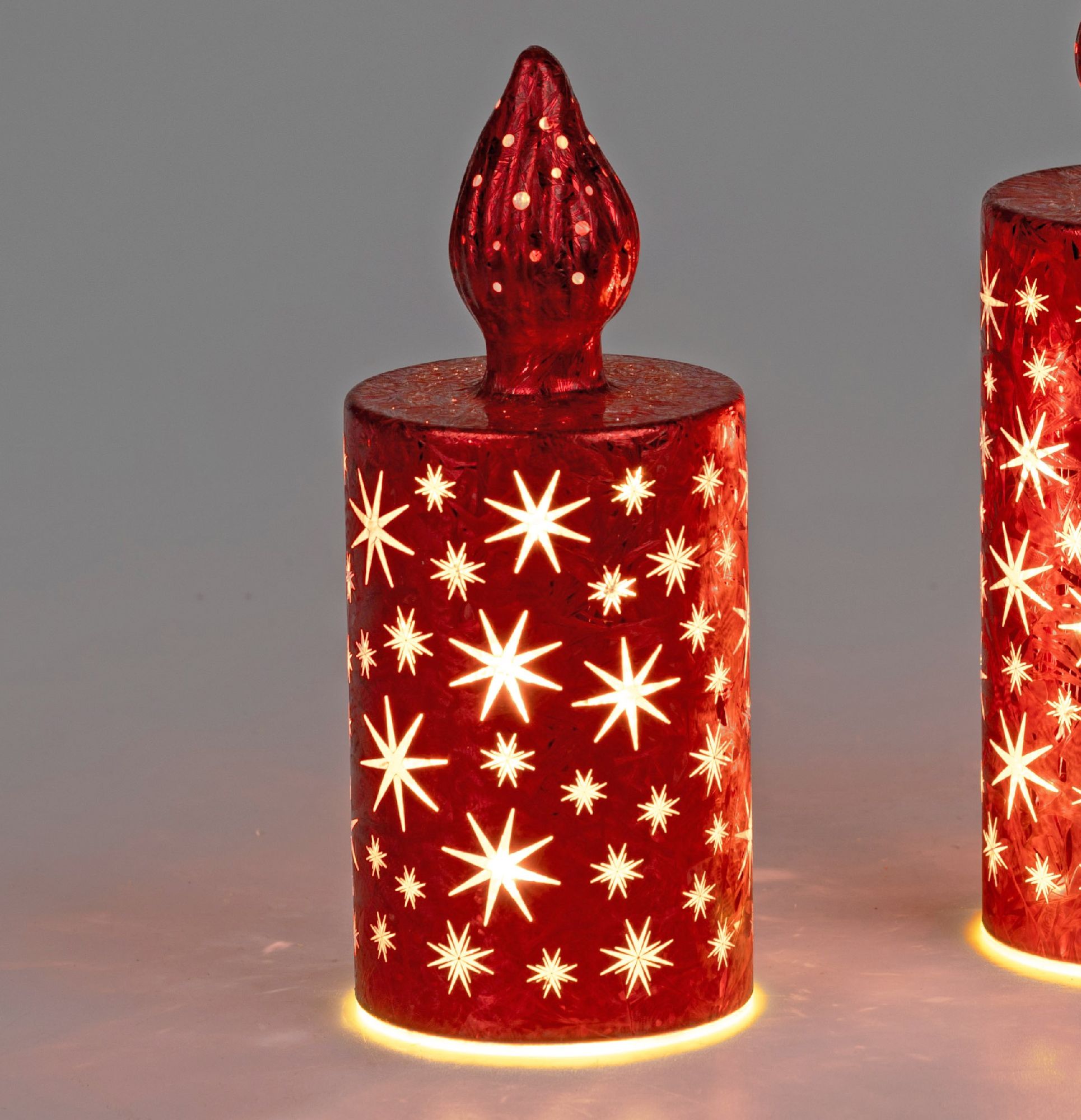 Rote Kerzen mit sternförmigen Mustern und leuchtendem Rand, auf einem neutralen Hintergrund.