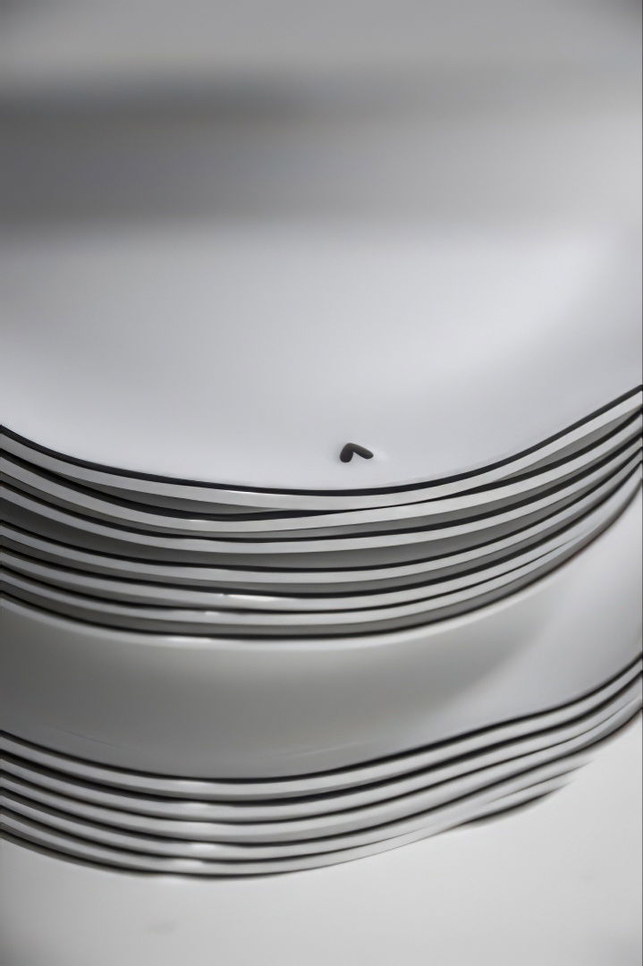 Gestapelte weiße Teller mit schwarzen Linien am Rand, einer der Teller hat eine kleine, abgerundete Vertiefung.
