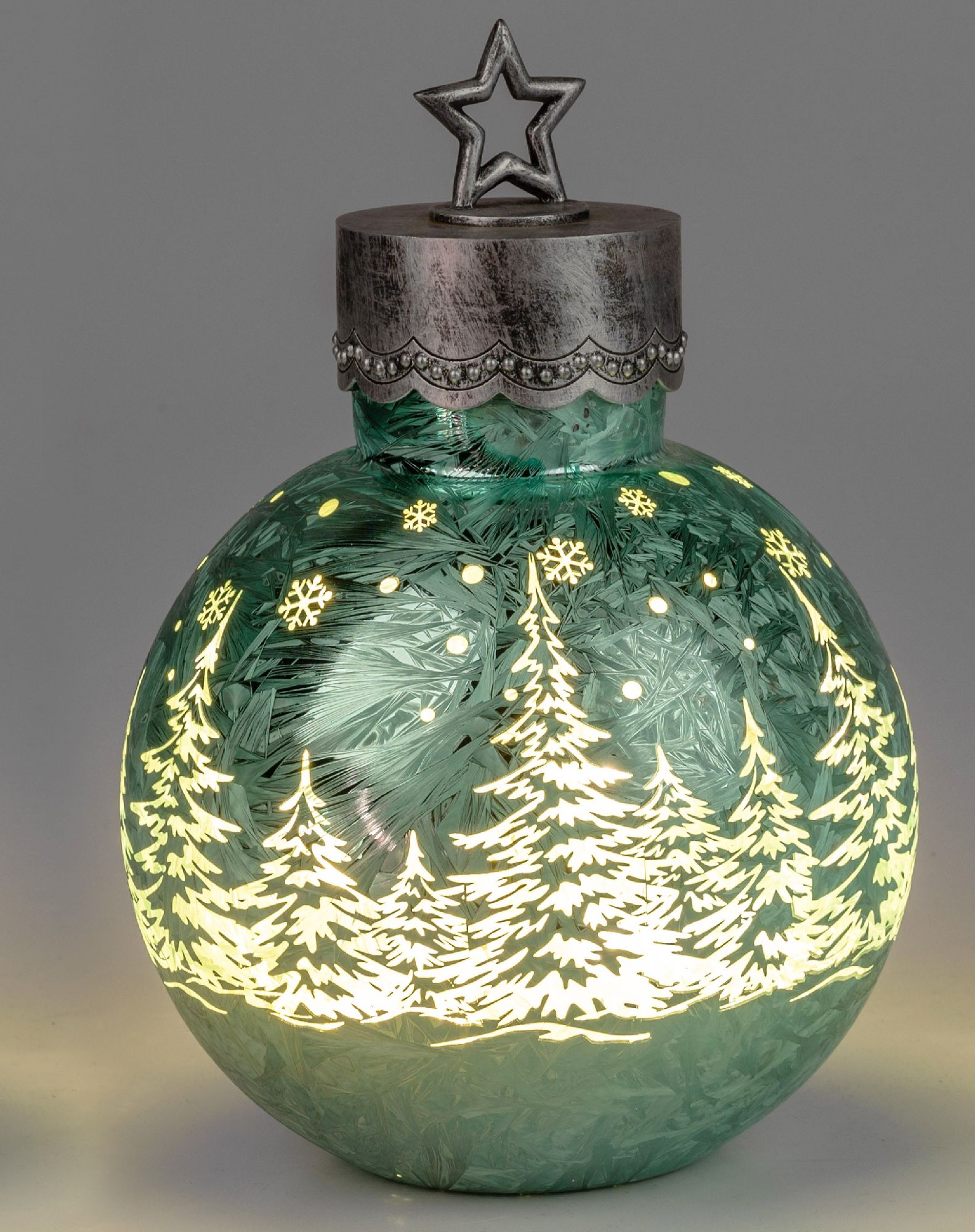 Grüne Weihnachtskugel mit beleuchteten Tannenbäumen und Schneeflocken, oben mit einem silbernen Ster