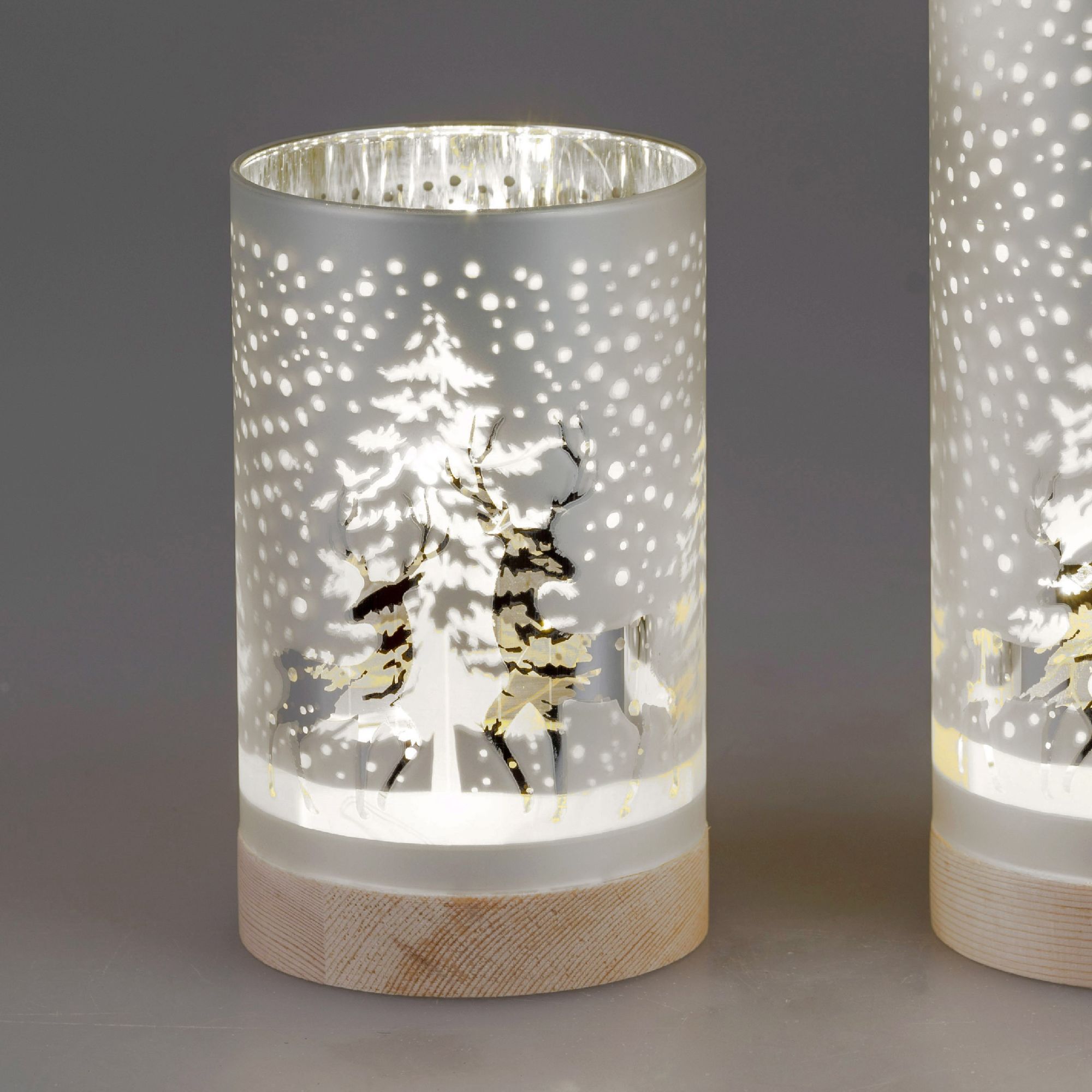 Zwei dekorative Gläser mit winterlichen Motiven von Bäumen und Rehen, beleuchtet und mit einem Holzs
