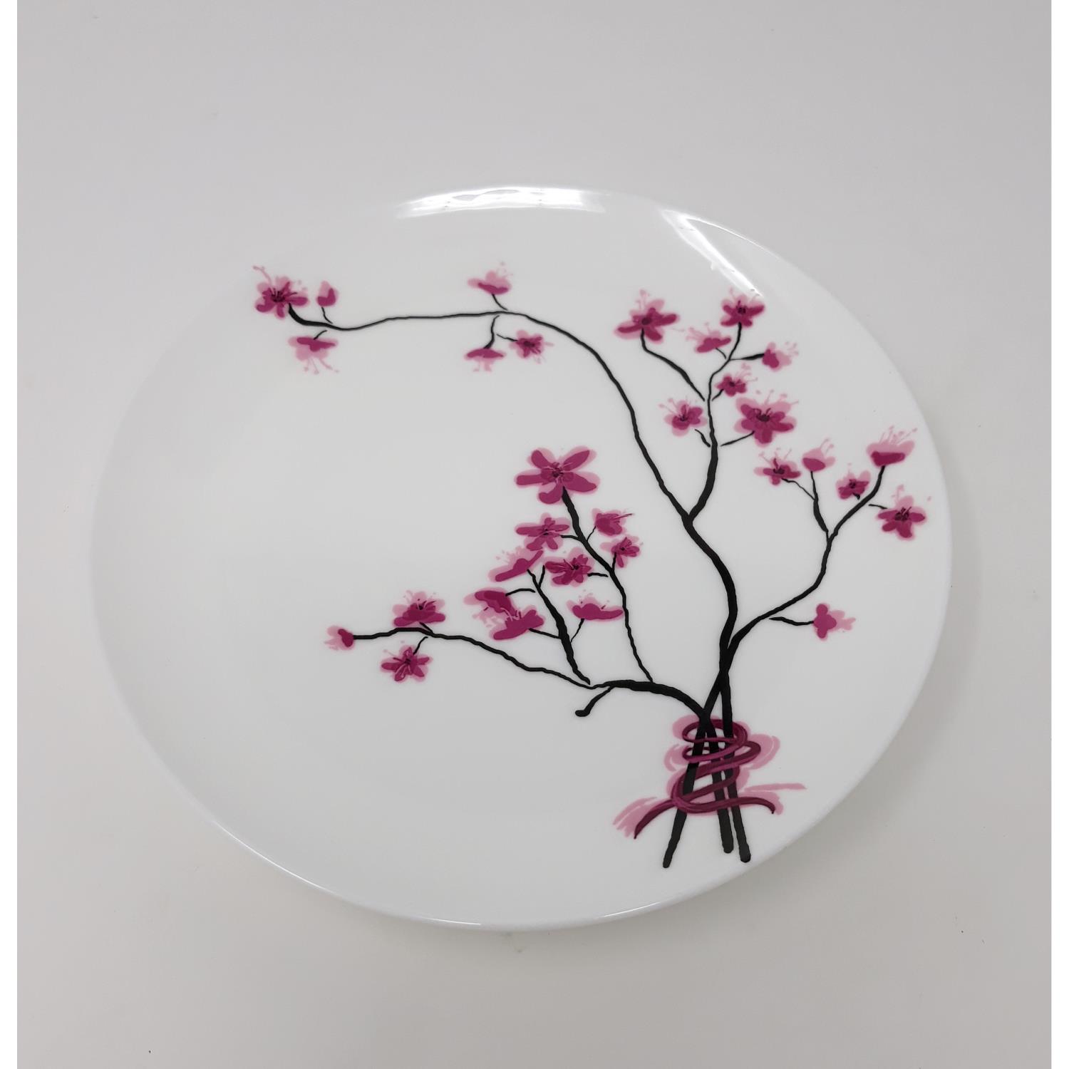 Weißer Teller mit pinken Blüten und schwarzen Ästen, die sich um einen Knoten winden. Hintergrund ist einfarbig.