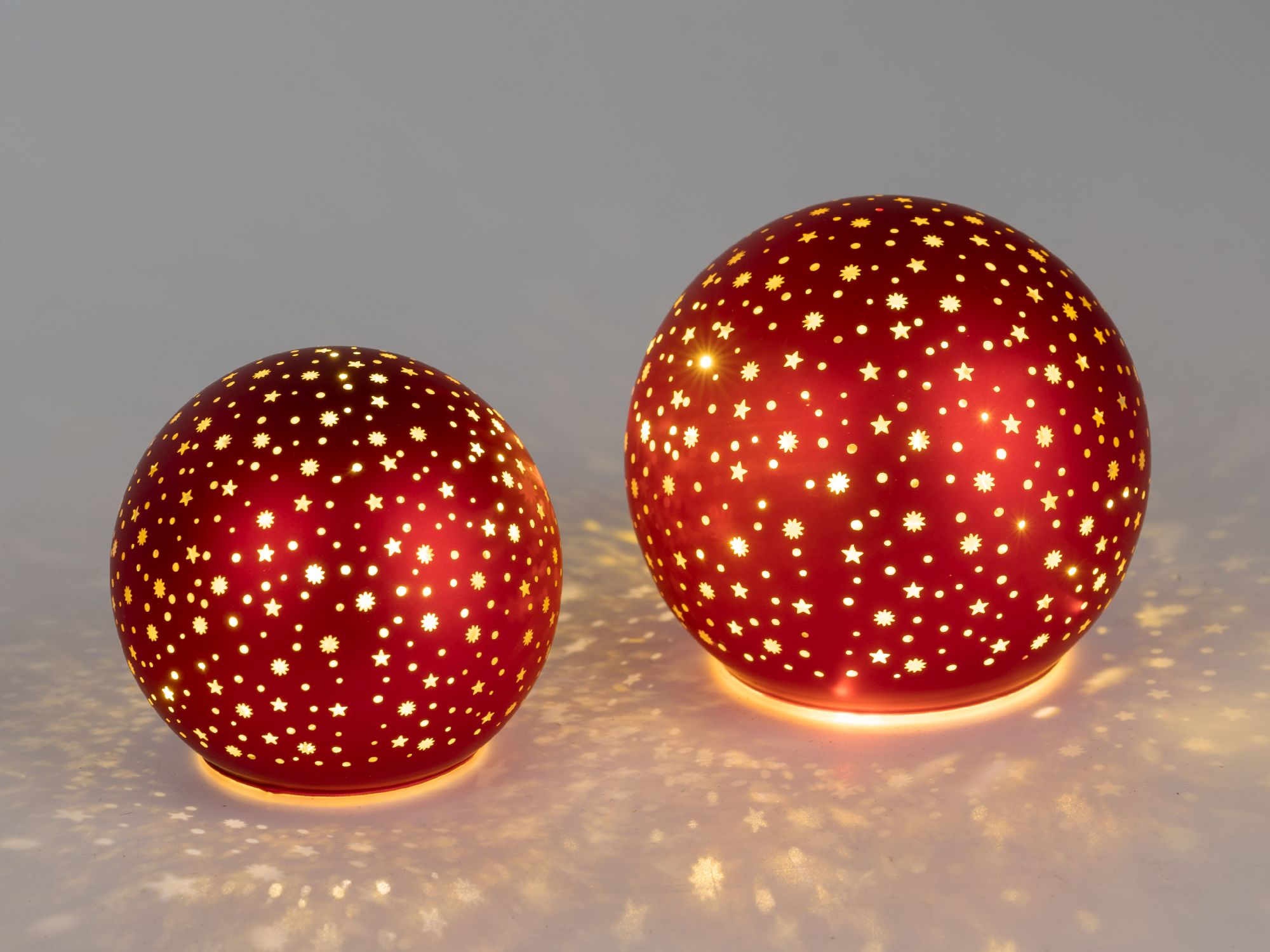Zwei rote, kugelförmige Objekte mit sternförmigen Ausschnitten, die warmes Licht abstrahlen und Scha
