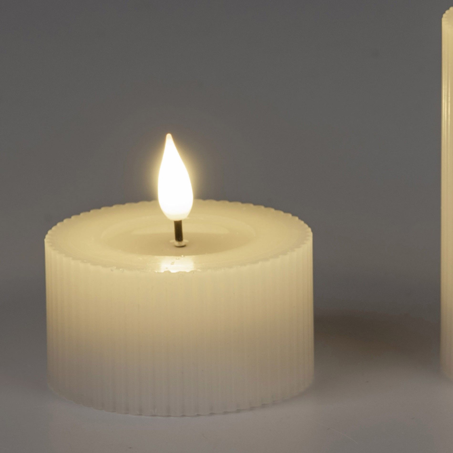 Zwei weiße Kerzen mit einer flackernden Flamme, eine mit gerillter Oberfläche, die andere glatt, vor