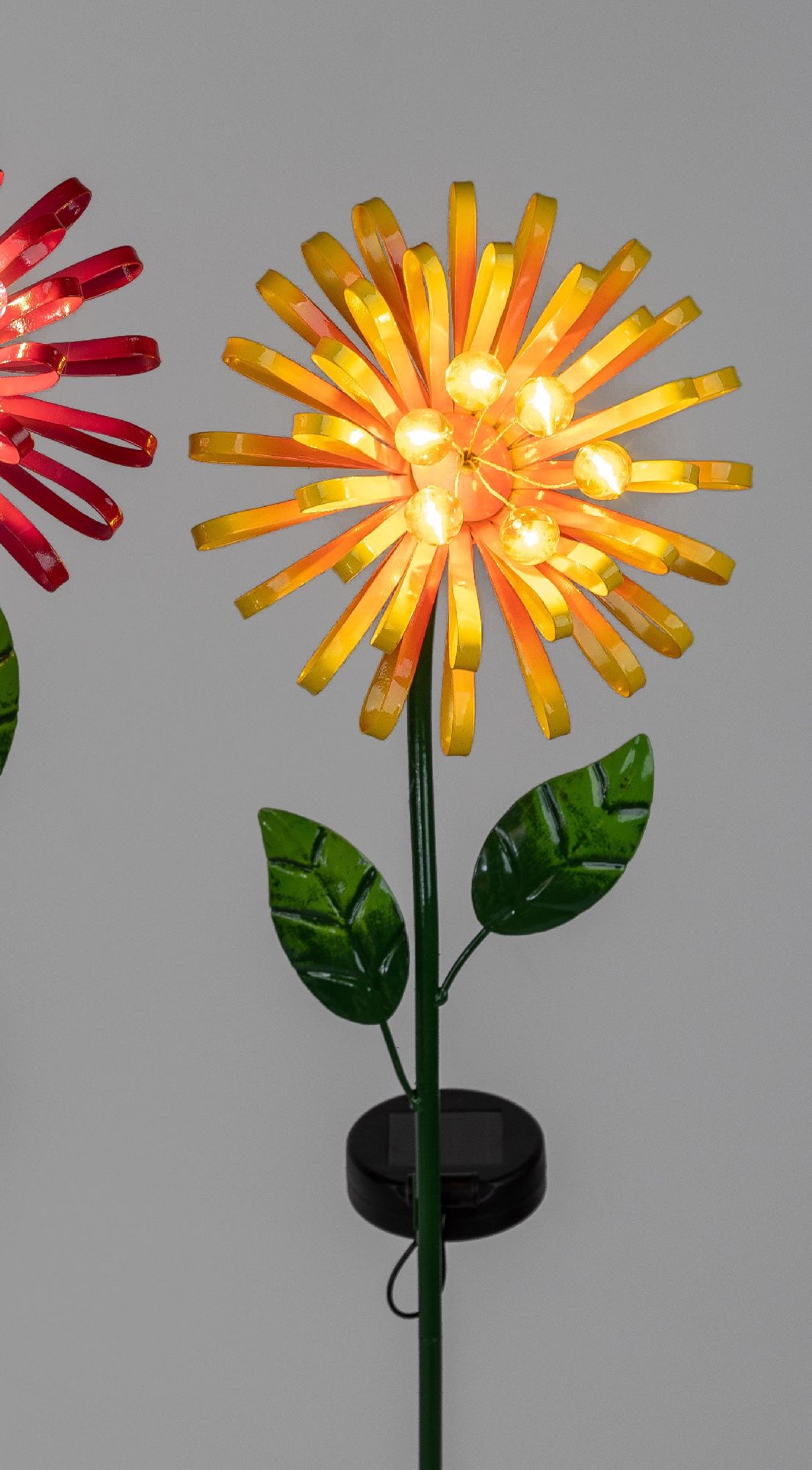 Bunte, leuchtende Blumen aus Kunststoff mit gelben und roten Blütenblättern und grünen Blättern, auf einem stabilen Stängel.