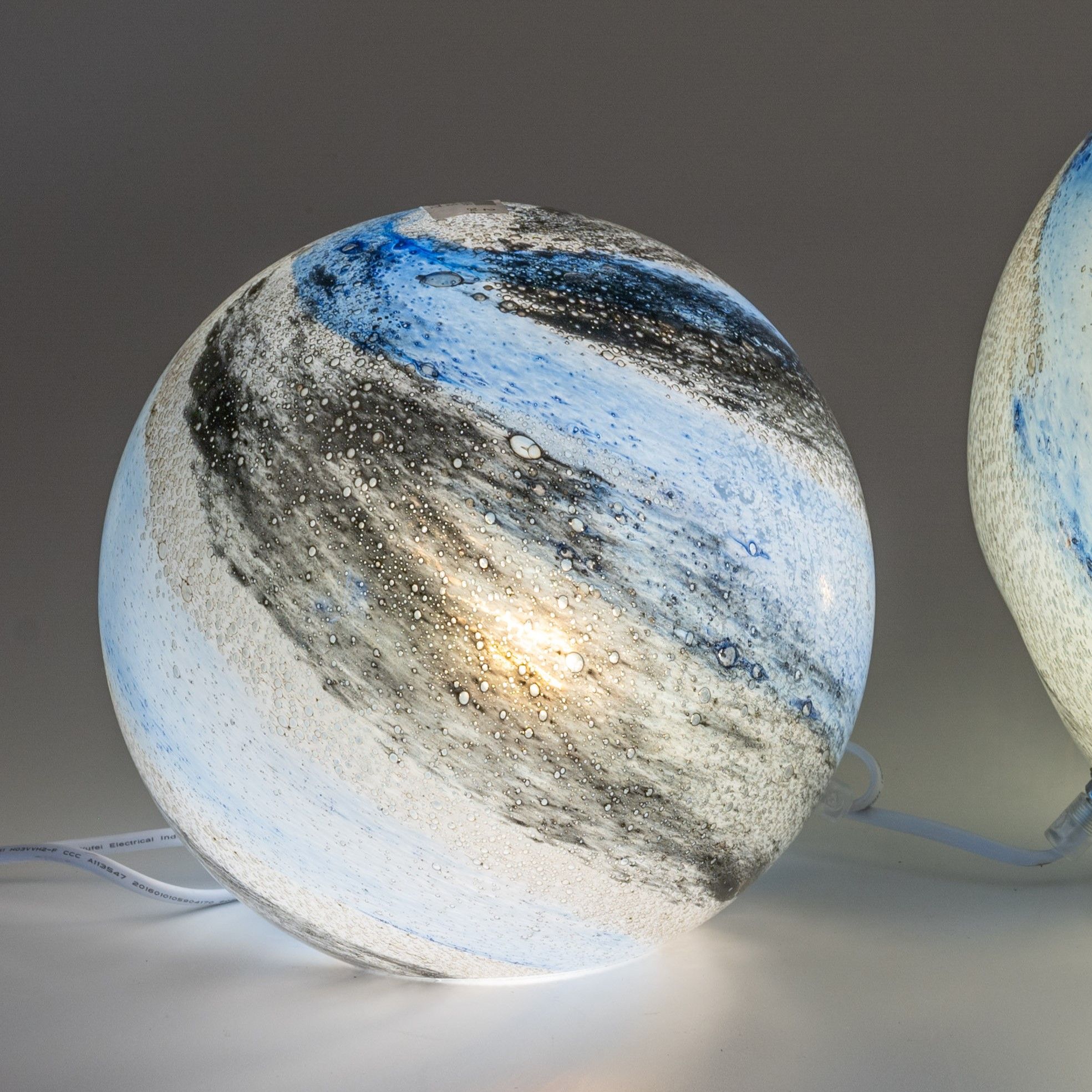 Runde Lampe mit blauen, schwarzen und weißen Farbschichten sowie Blasen, die Licht abstrahlen. Kabel sichtbar.