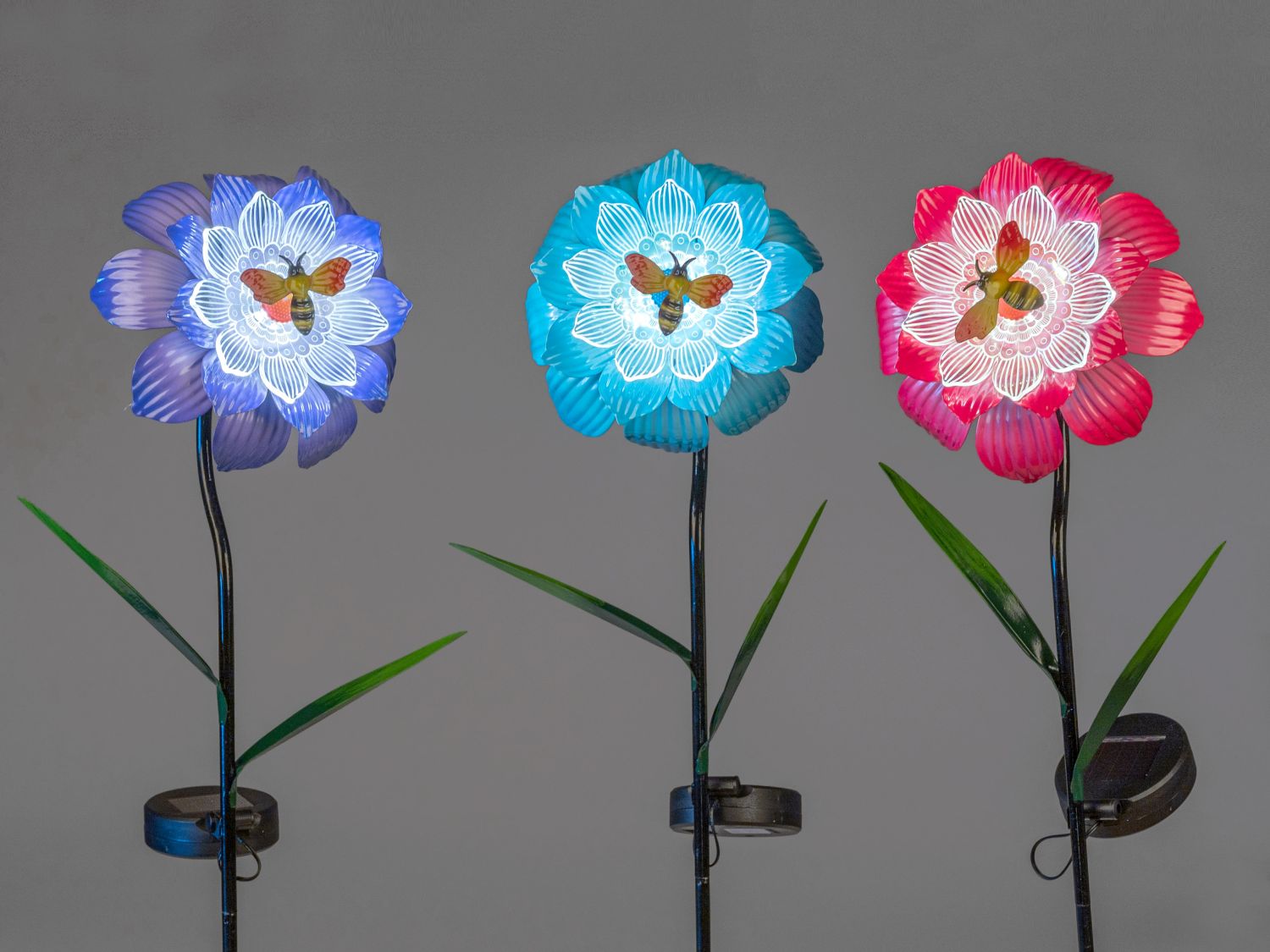 Drei leuchtende Kunstblumen in Blau, Türkis und Pink mit Schmetterlingen vor grauem Hintergrund