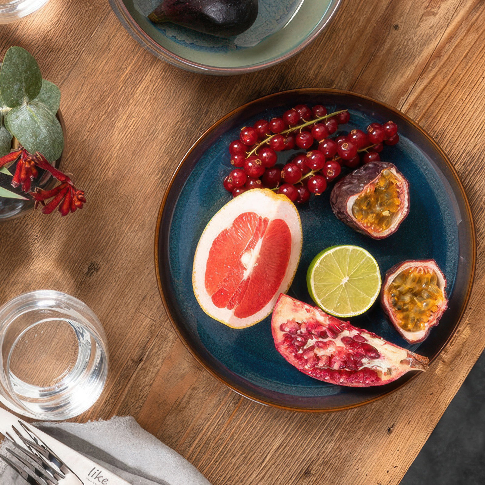 Ein Teller mit verschiedenen Früchten: Grapefruit, Limette, Passionsfrucht, Granatapfel und rote Johannisbeeren. Holzuntergrund.