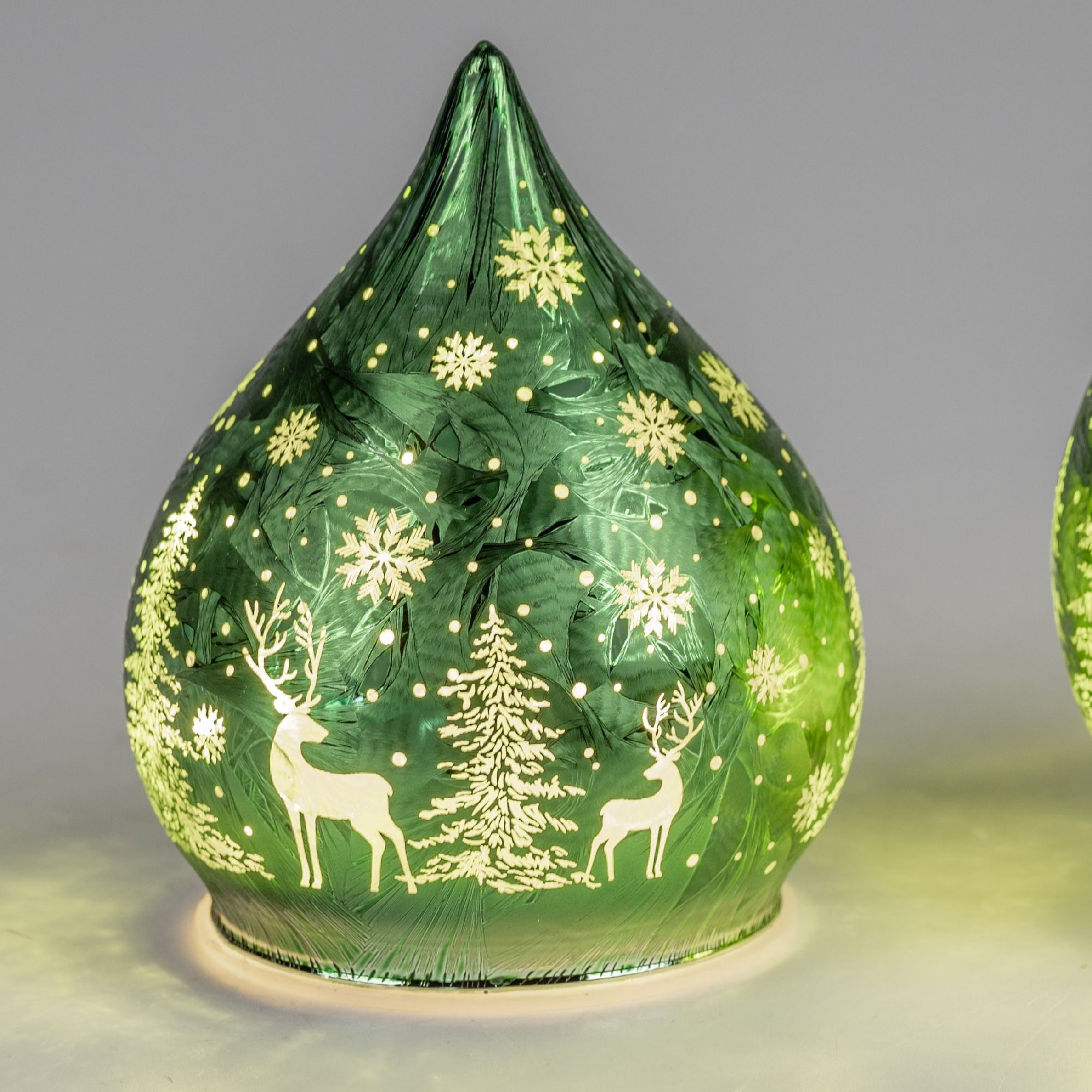 Grüne, gläserne Weihnachtsdekoration in Tropfenform mit weißen Schneeflocken, Tannenbäumen und Renti