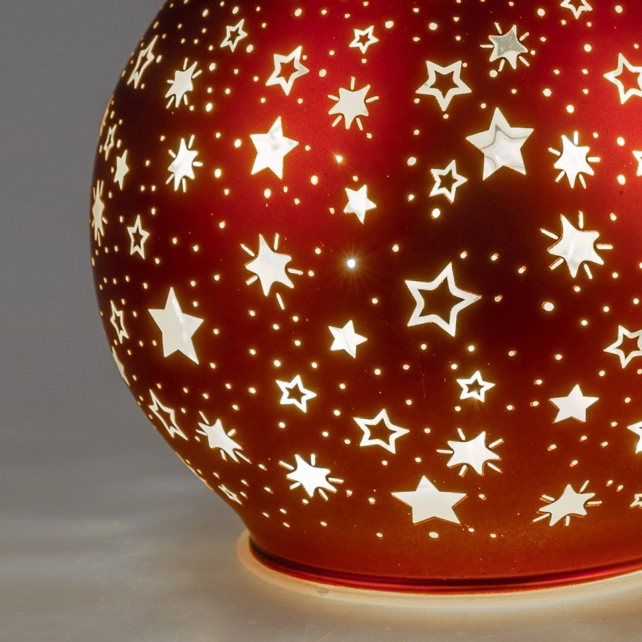 Runde, rote Lampe mit durchbrochenen Sternenmustern, die Licht abstrahlen und einen dekorativen Effe