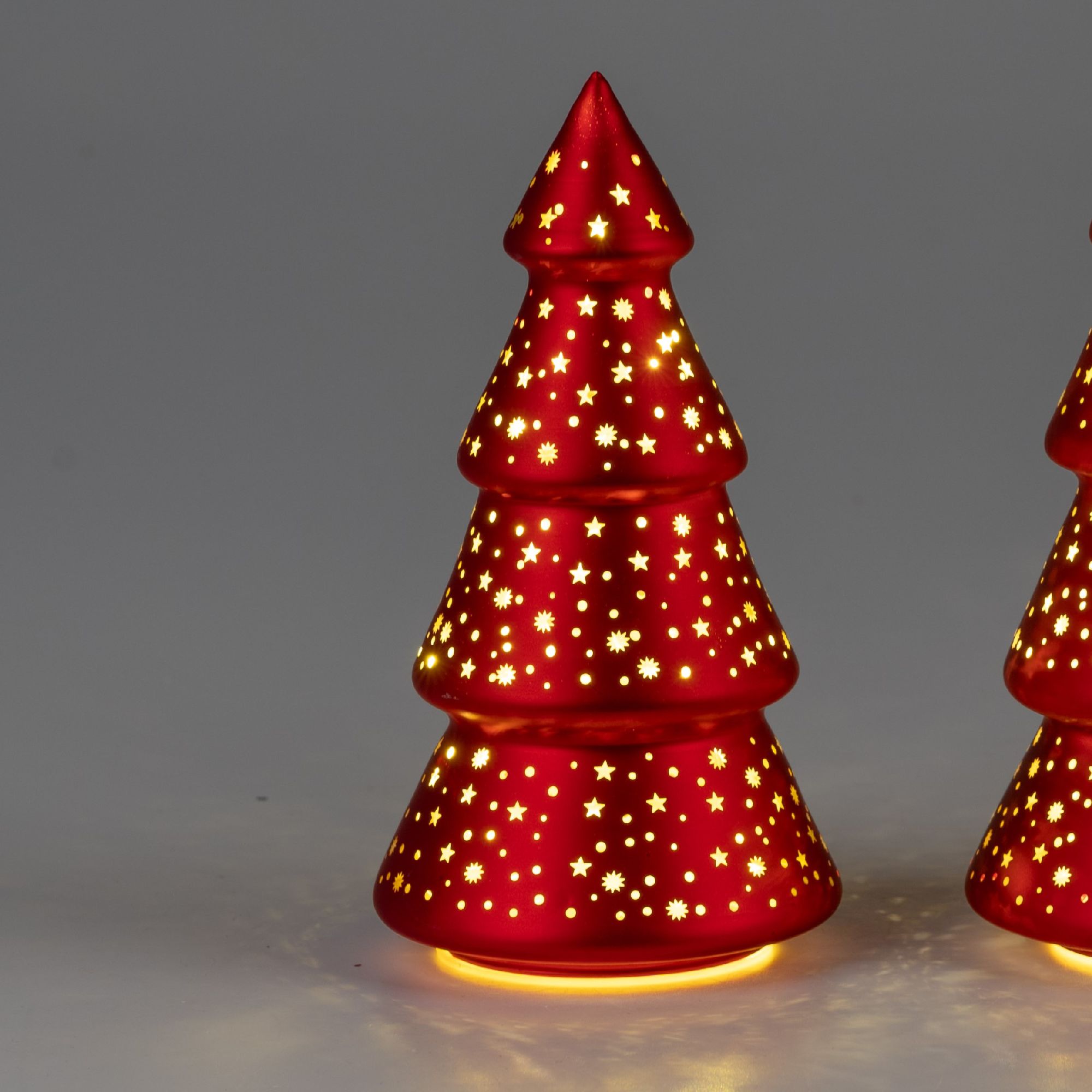 Roter Weihnachtsbaum aus Keramik mit Sternenmustern und beleuchtetem Sockel, vor neutralem Hintergru