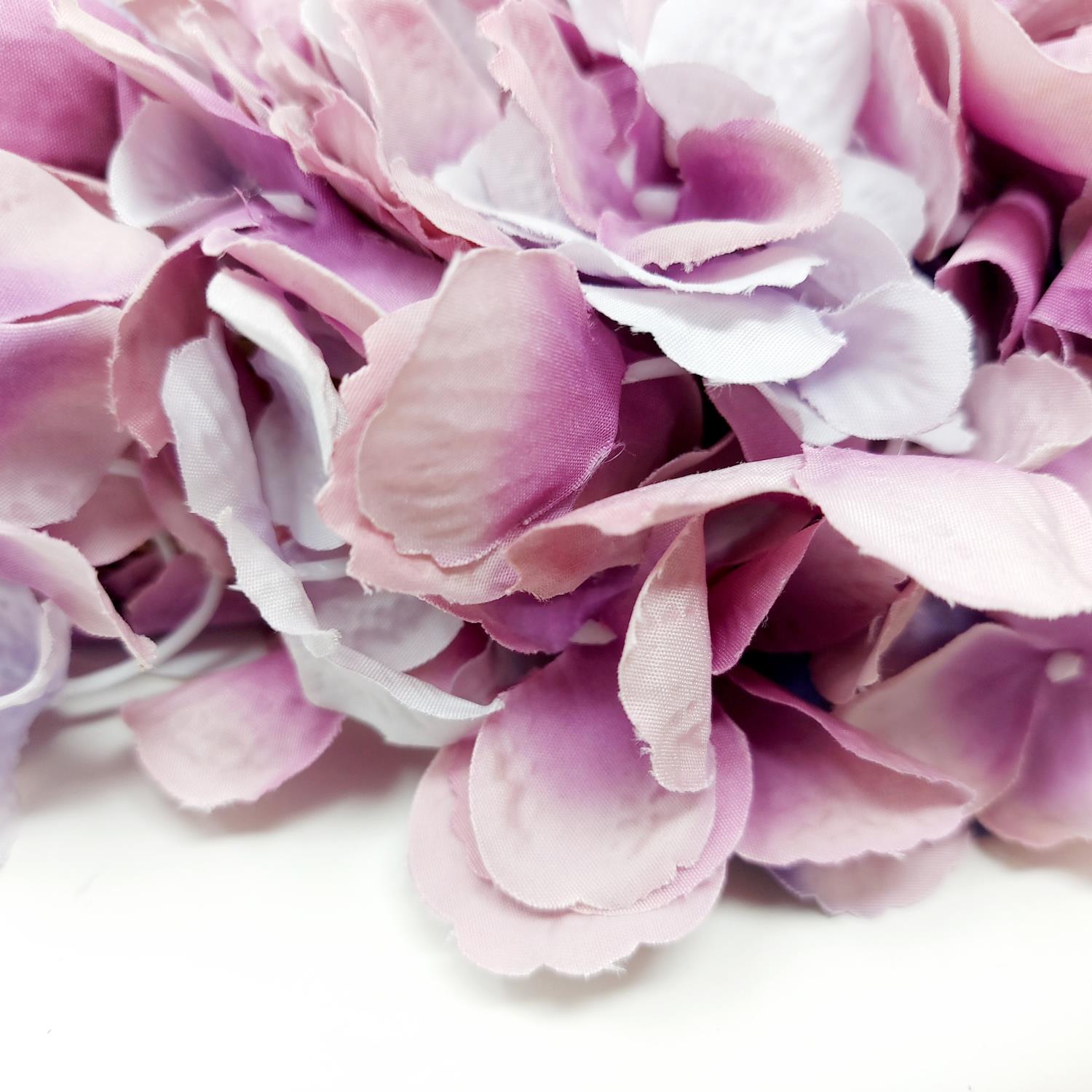 Bunte, künstliche Blütenblätter in verschiedenen Rosa- und Lilatönen, dicht zusammenliegend auf hell