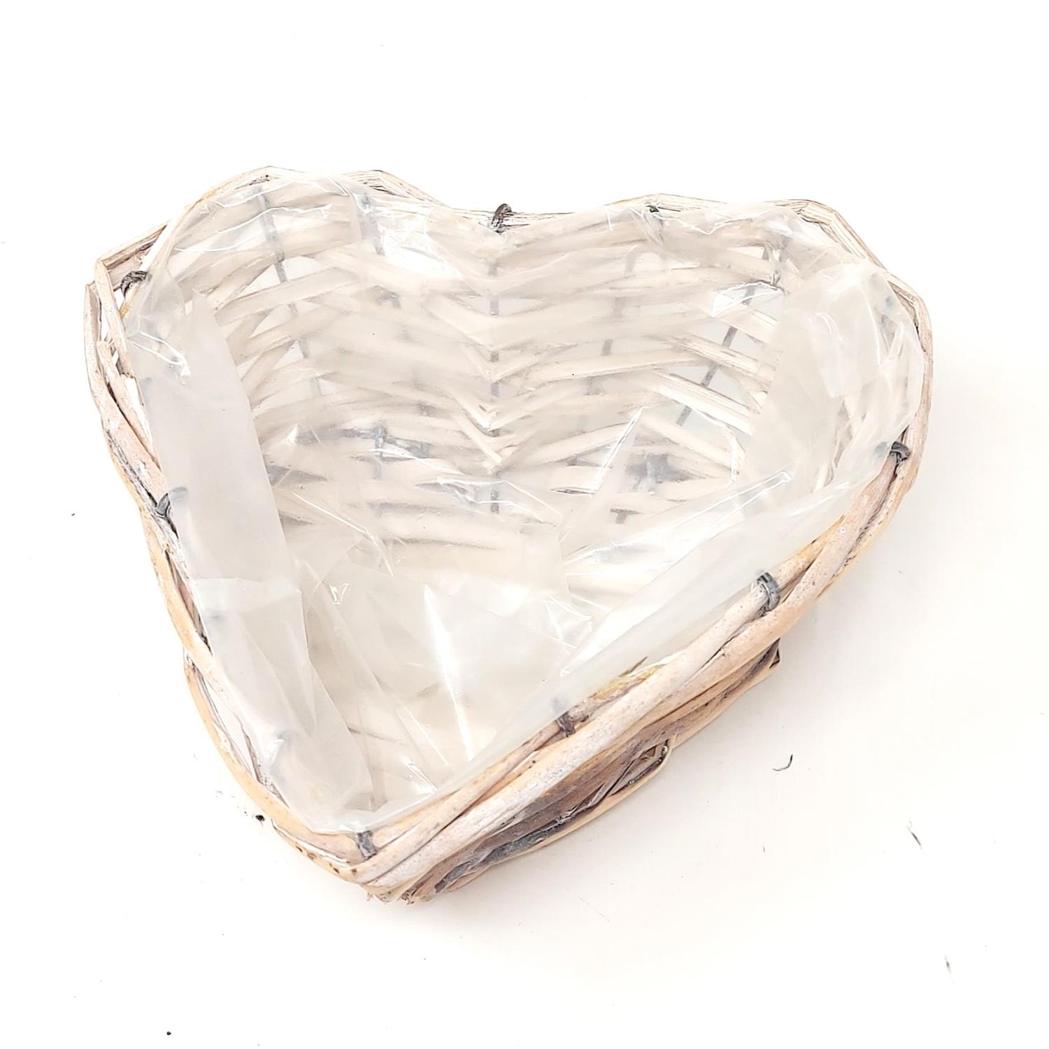 Ein herzförmiger Korb aus geflochtenem Material mit einer transparenten Innenauskleidung. Der Korb ist auf einem weißen Hintergrund platziert.