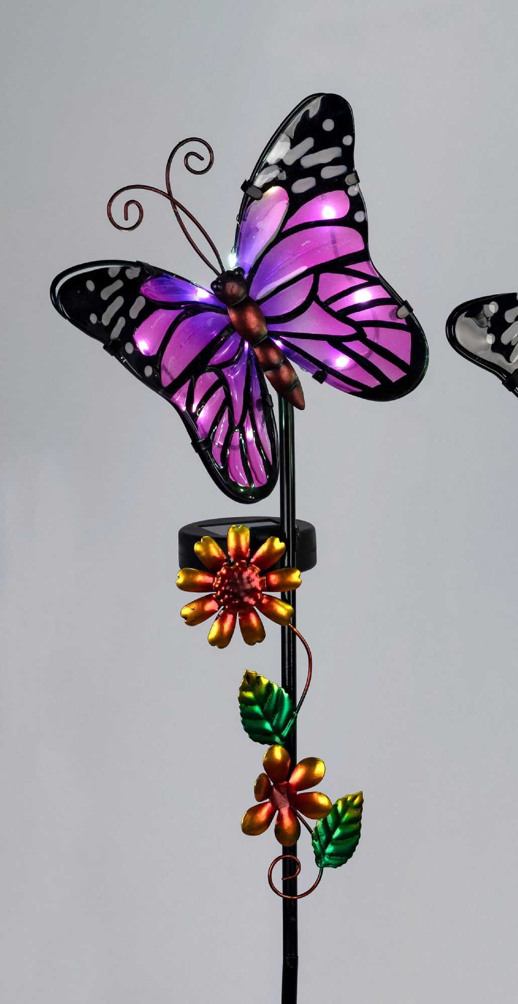 Bunte Metallfigur eines Schmetterlings mit lila Flügeln und einer Blume, auf einem Stab montiert. Hi