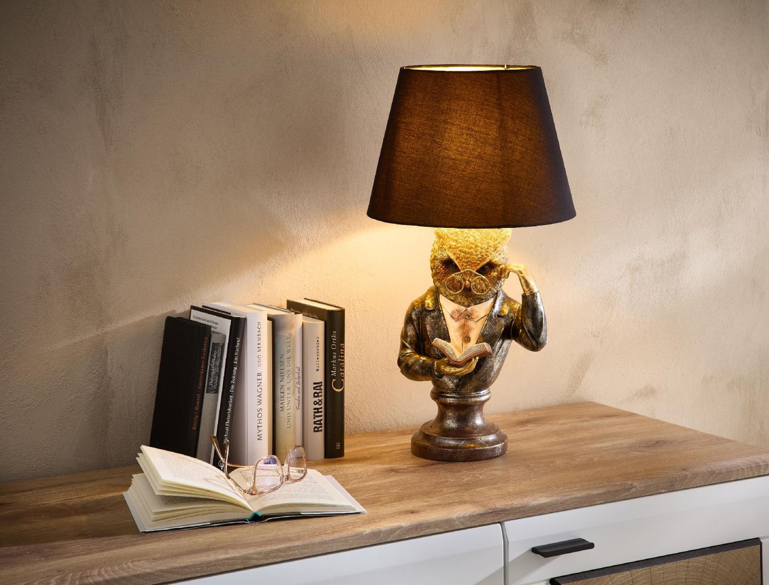 Eine Tischlampe in Form einer Figur mit Brille, die ein Buch hält, steht auf einem Holzregal neben m